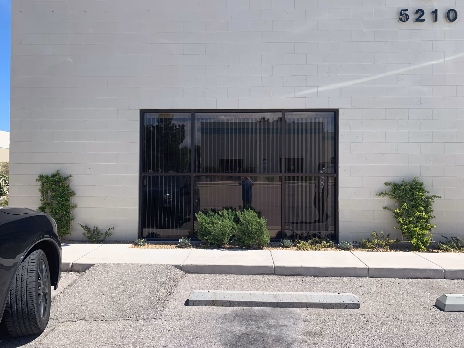 Front of a beige building with a large glass door and surrounding shrubs.