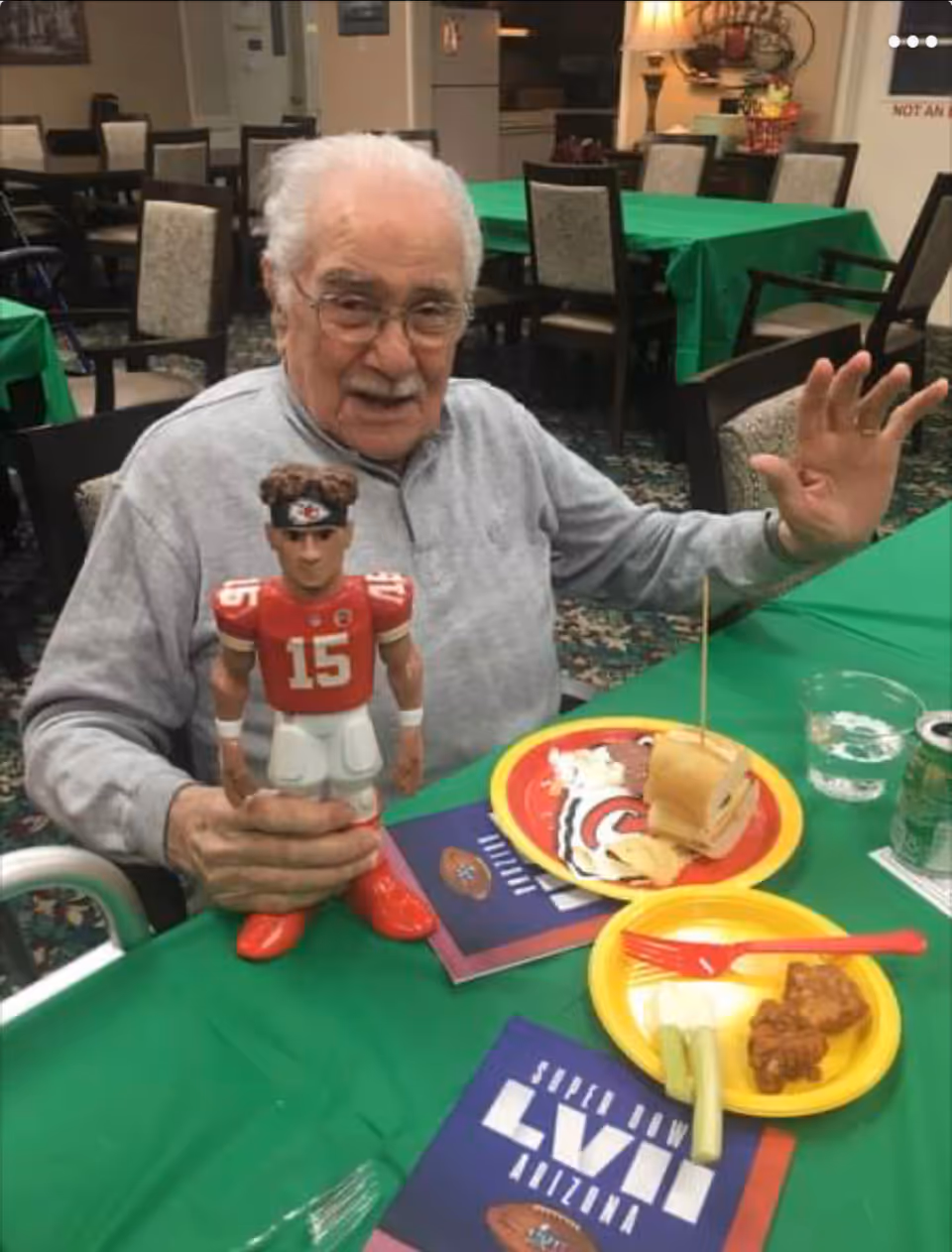 Elderly man at a green-draped dining table holds a football figurine.