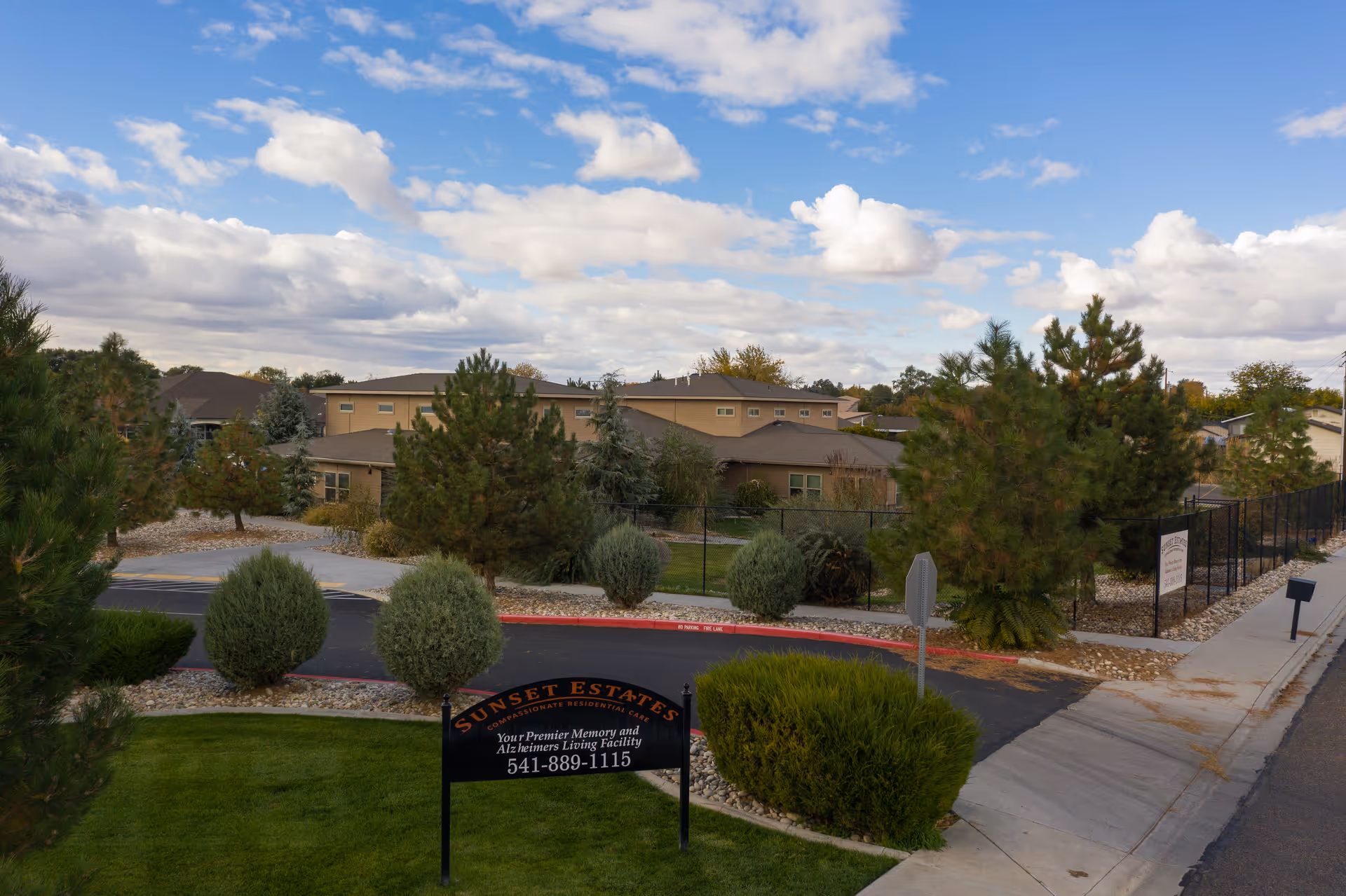 Exterior view of Sunset Estates and Villa senior living with a landscaped entrance and blue sky.