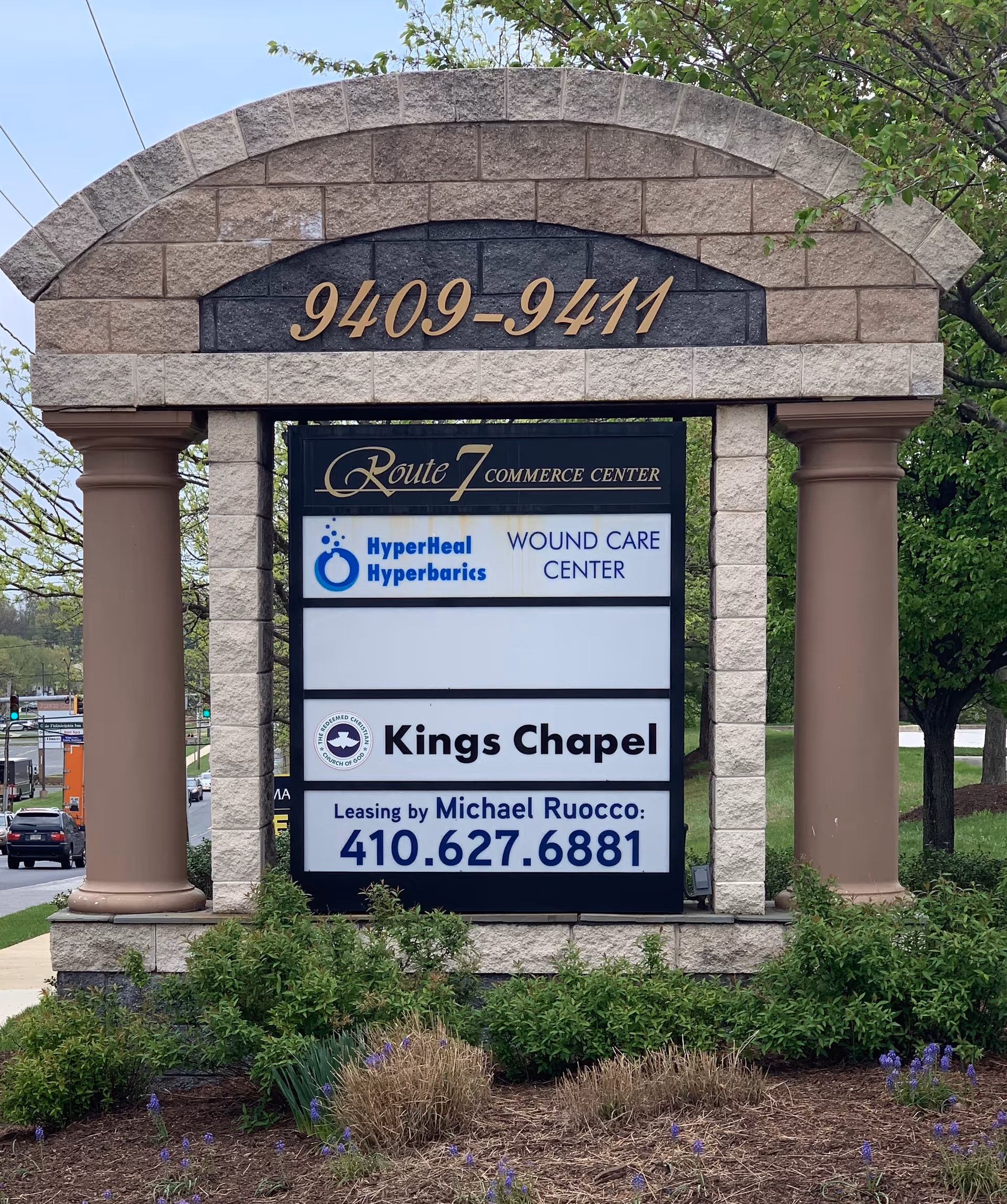 Stone entrance sign for Route 7 Commerce Center showing tenants and contact number.