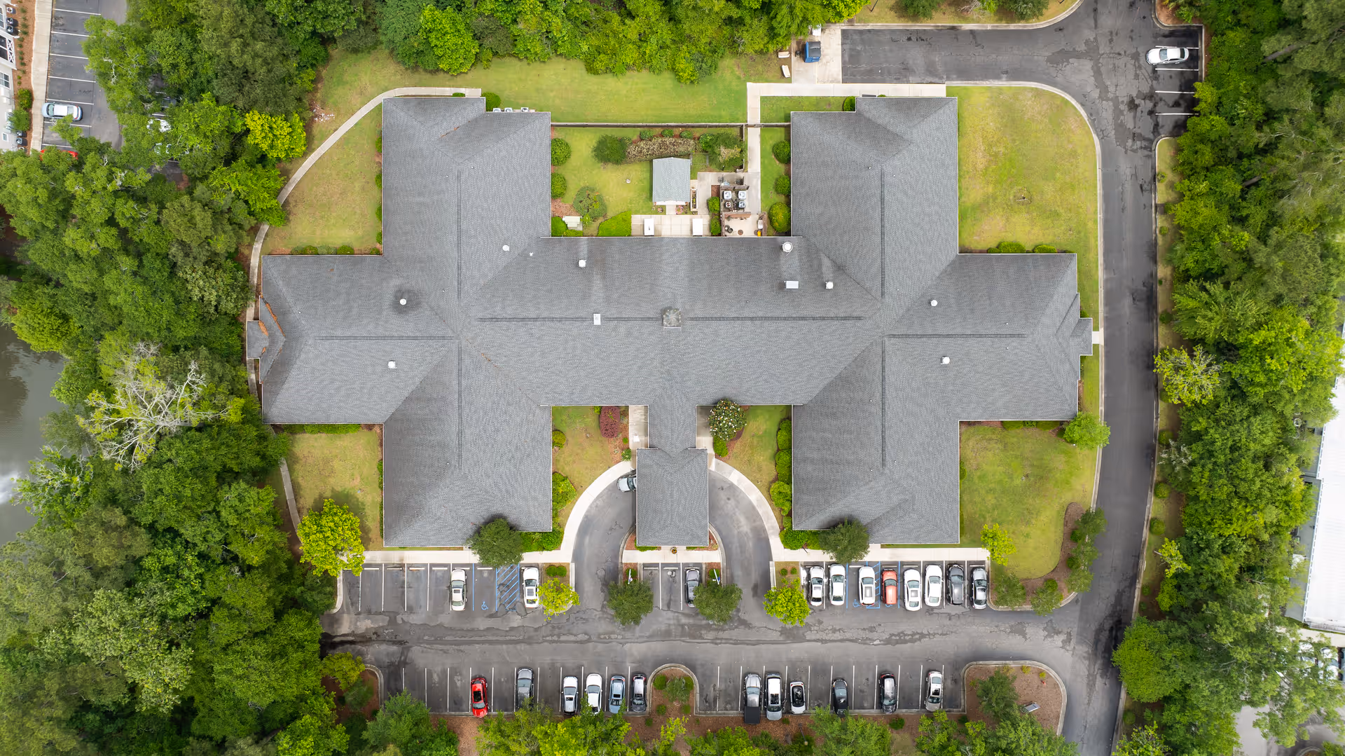 Aerial view of TerraBella Summerville senior living facility showing the building's roof, surrounding parking lots with parked cars, green lawns, trees, and pathways.