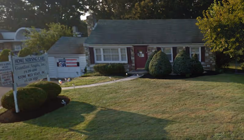 Single-story facility with front door, manicured lawn, and Guardian Angels home health sign.