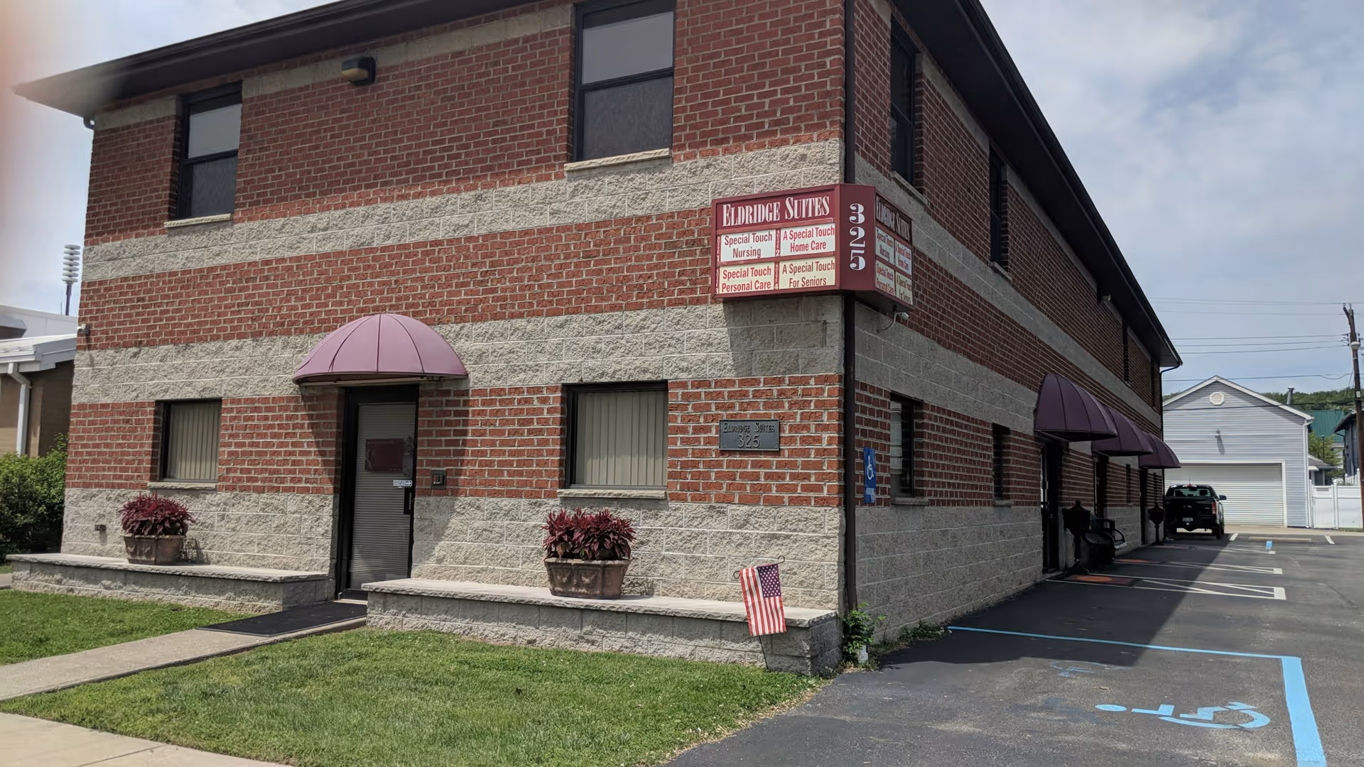 Two-story brick senior living building with purple awnings and a parking lot.