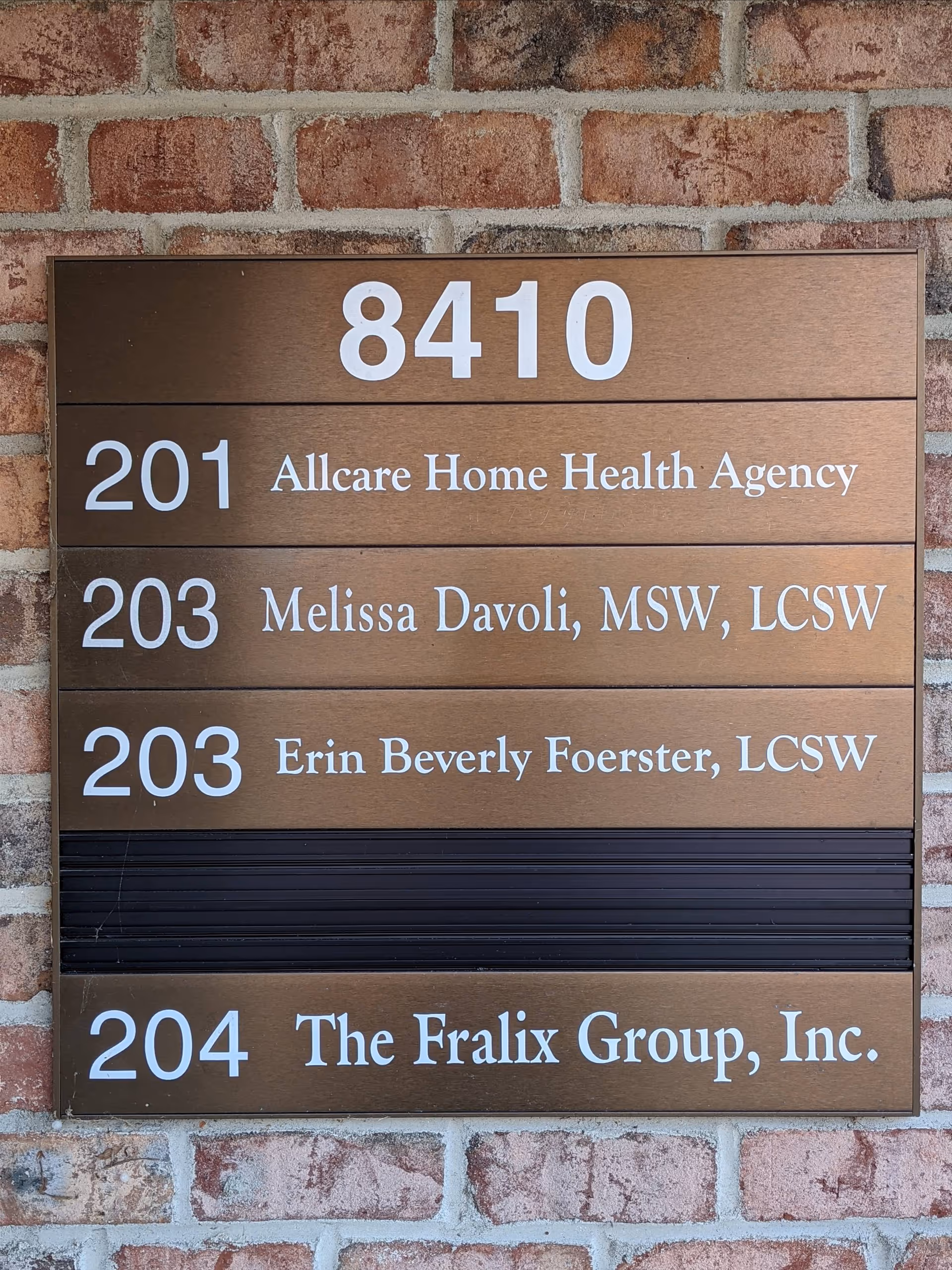 Brown directory sign on a brick wall lists room numbers and facility names.