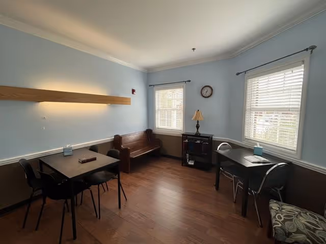 Light blue lounge area with two tables, chairs, bench, and windows in Abbey Hospice.