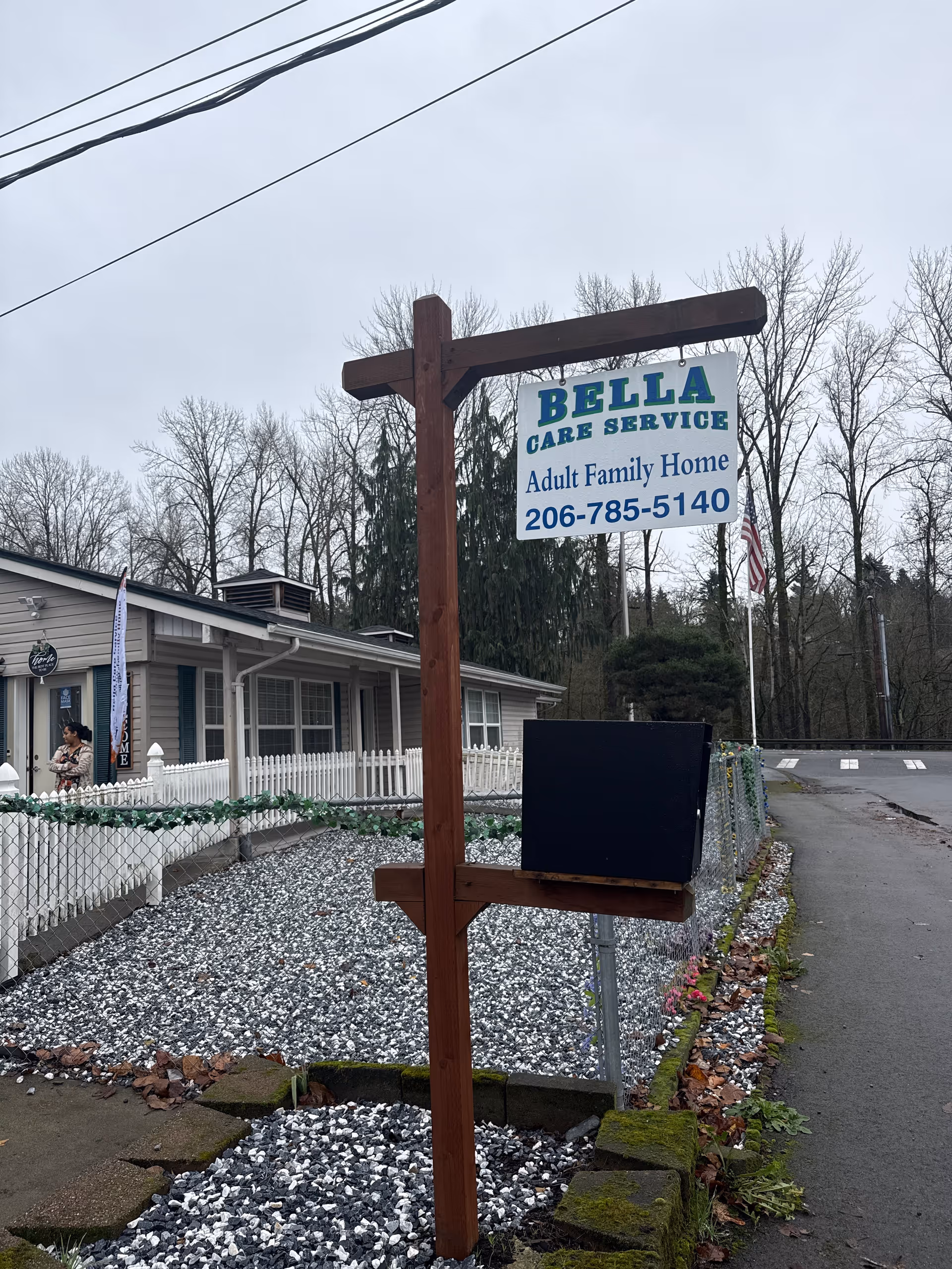 Exterior view of Bella Care Service Adult Family Home sign beside gravel yard and building.