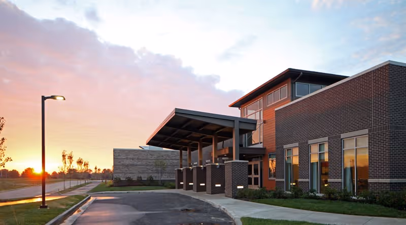 Wellbrooke of Avon senior living building with brick facade, covered entrance, and sunset sky.