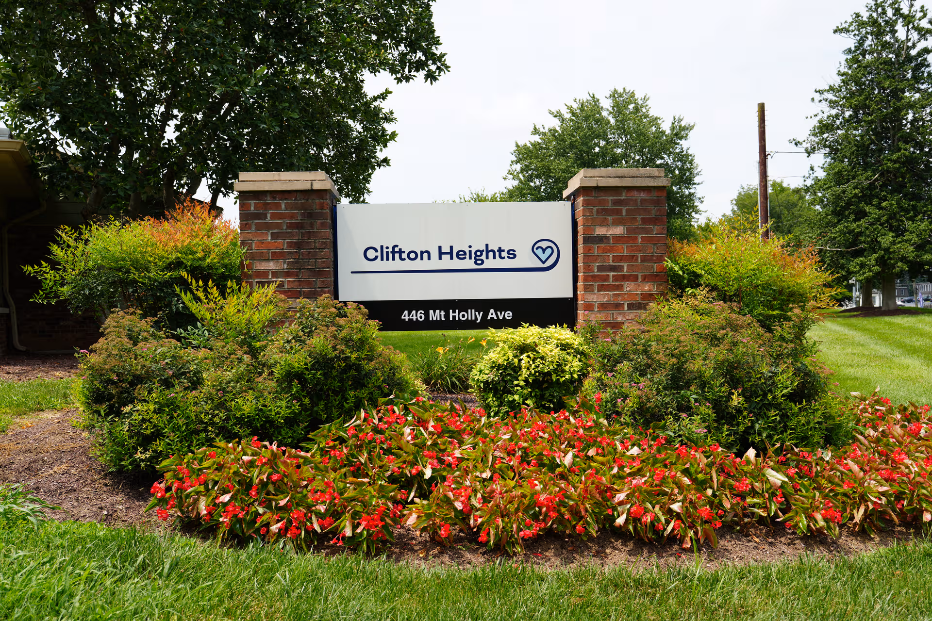 Entrance sign for Clifton Heights, surrounded by shrubs and colorful flower beds.