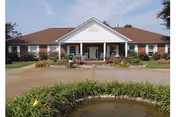 Single-story brick senior living facility with a covered entrance and a pond in front.