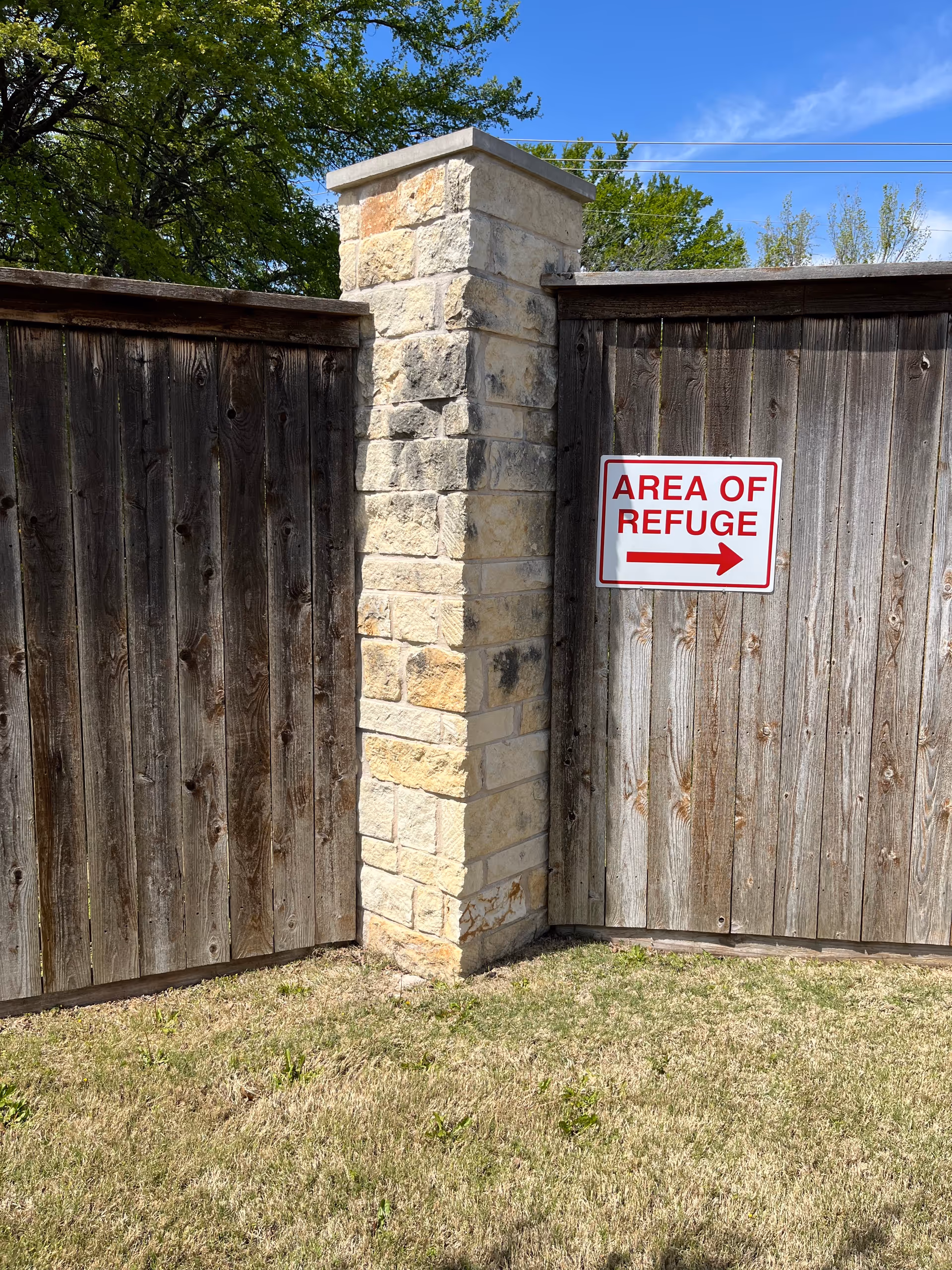 Stone pillar between weathered wooden gates with an Area of Refuge sign outdoors.