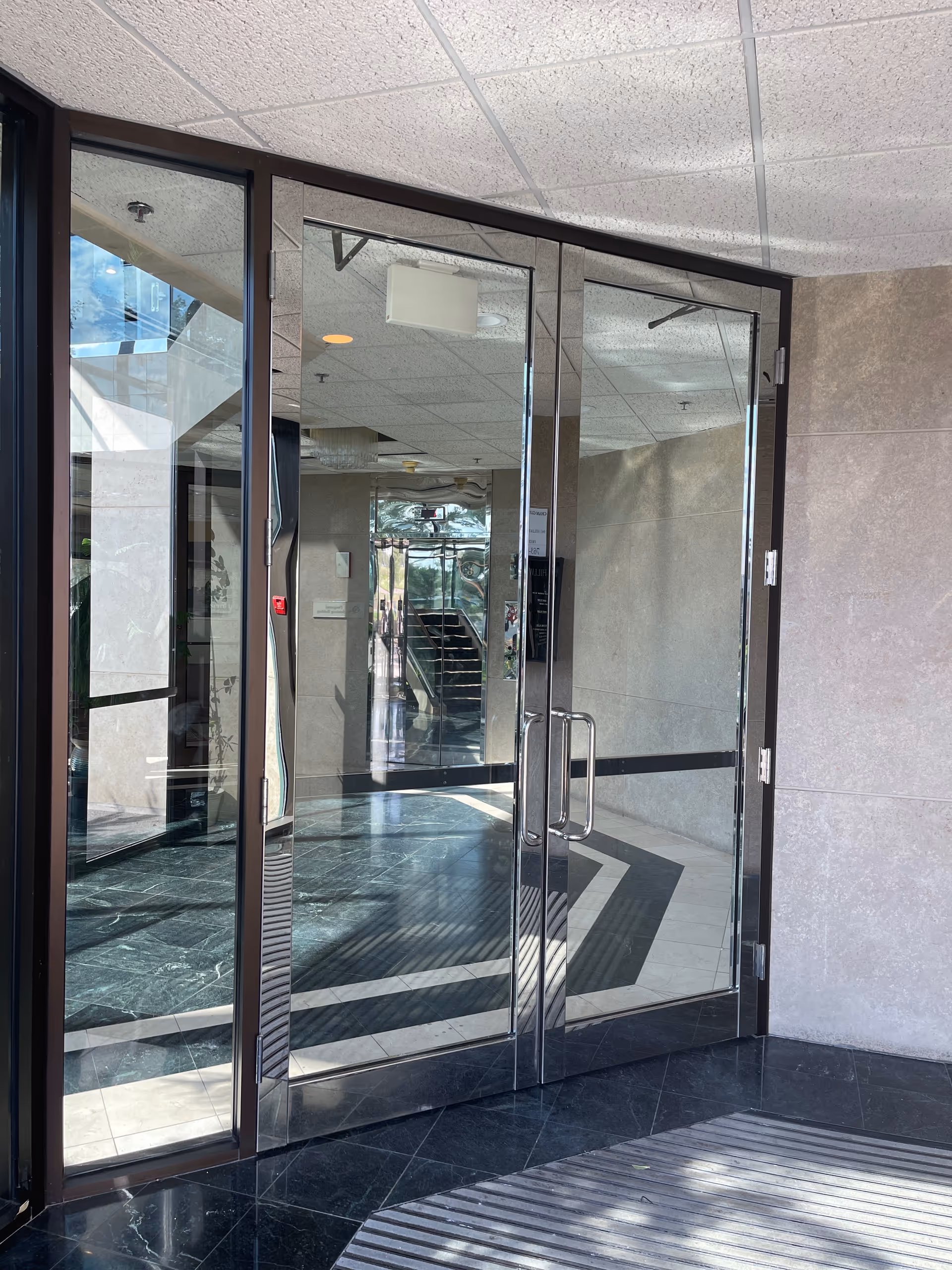 Glass double doors lead into a modern lobby with tiled floors and reflections.