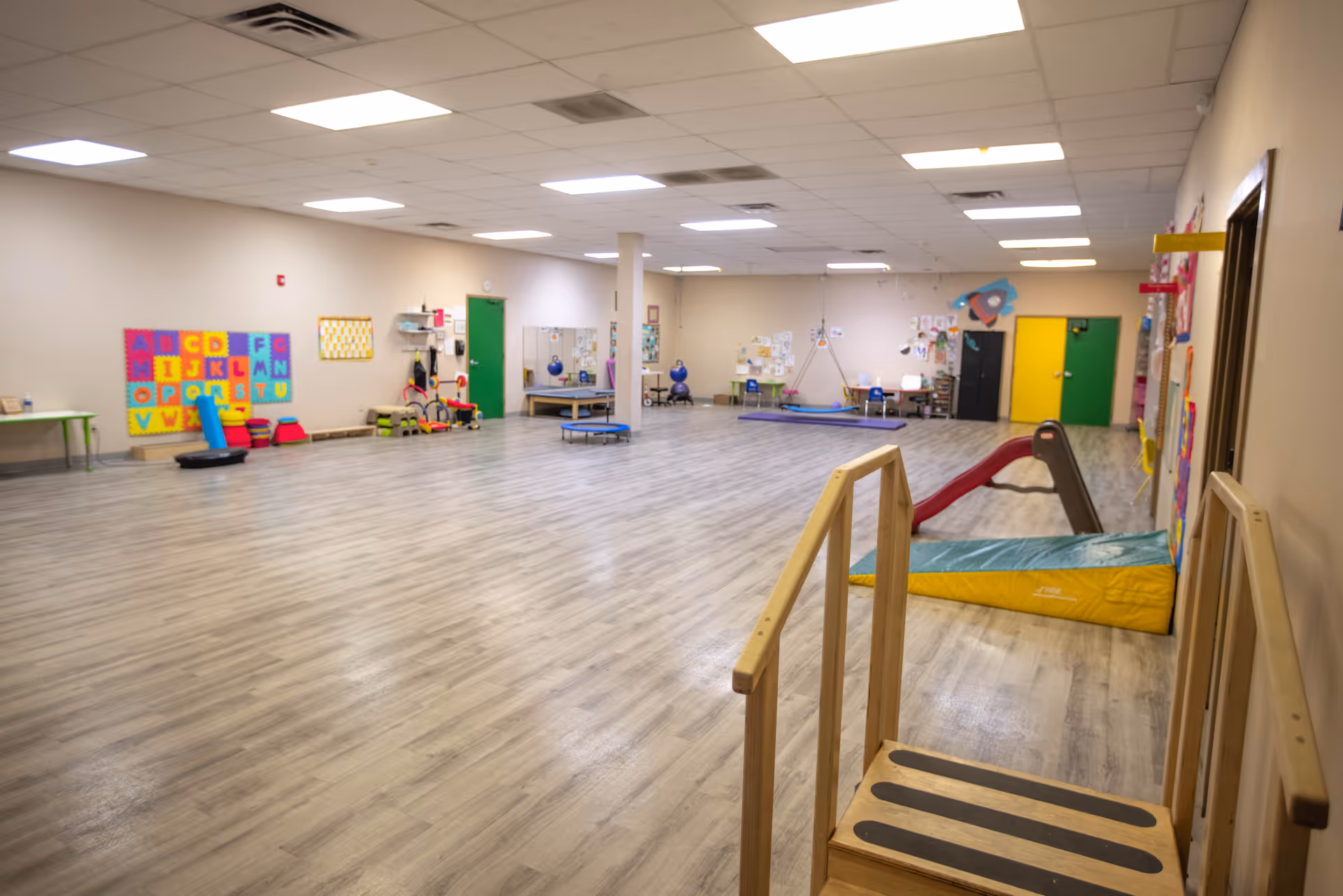 Spacious indoor activity room with colorful play equipment and a wooden ramp.