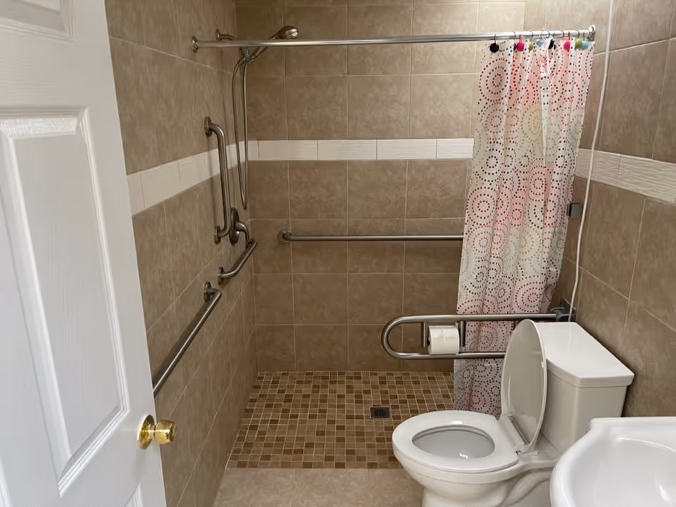 Accessible bathroom with grab bars, a shower curtain, and a toilet.