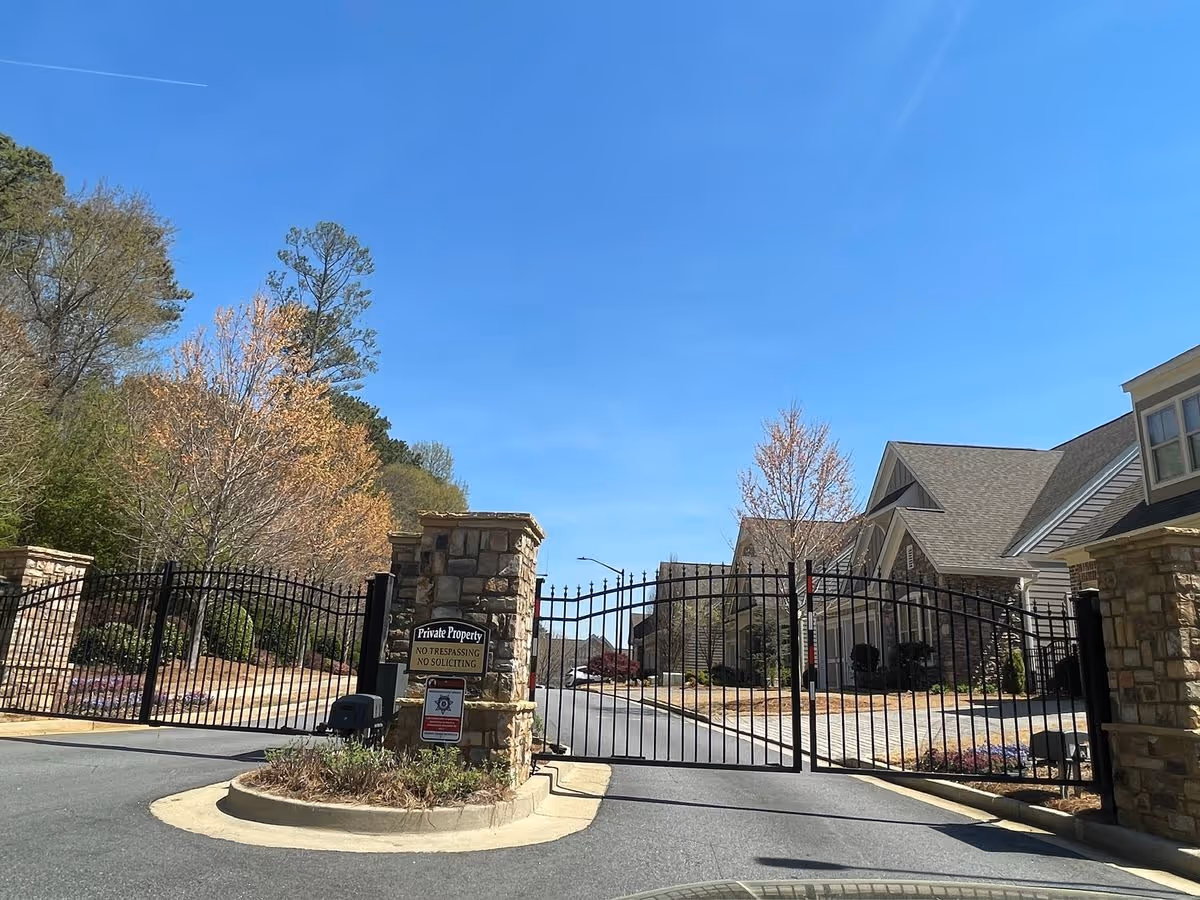 Wrought-iron gated entrance with stone pillars leading into a residential community under a clear blue sky.