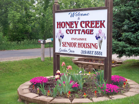 Sign for Honey Creek Cottage Senior Housing surrounded by flowers and greenery.