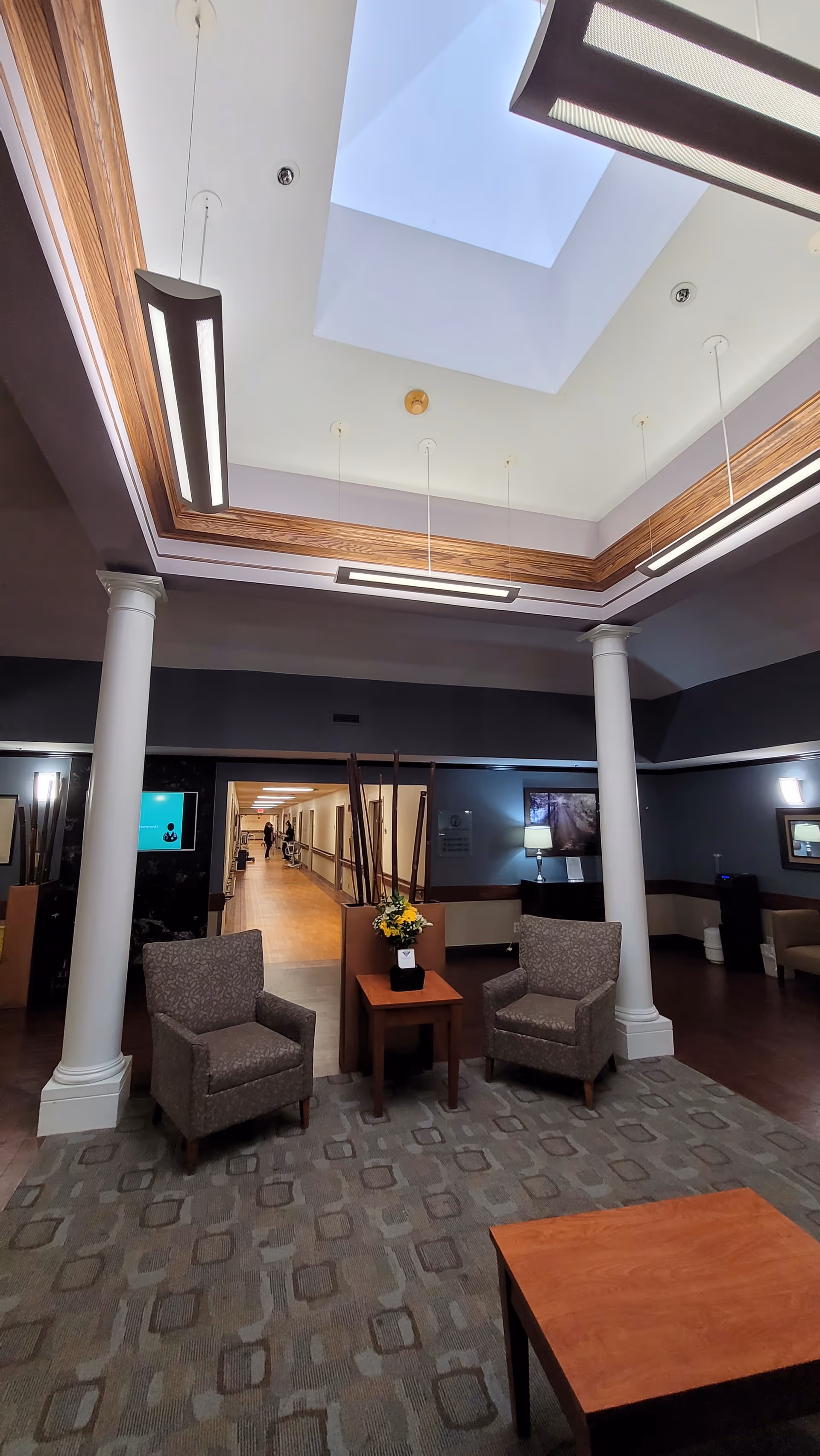 Interior lobby with two chairs, a table with flowers, pillars, and a skylight.