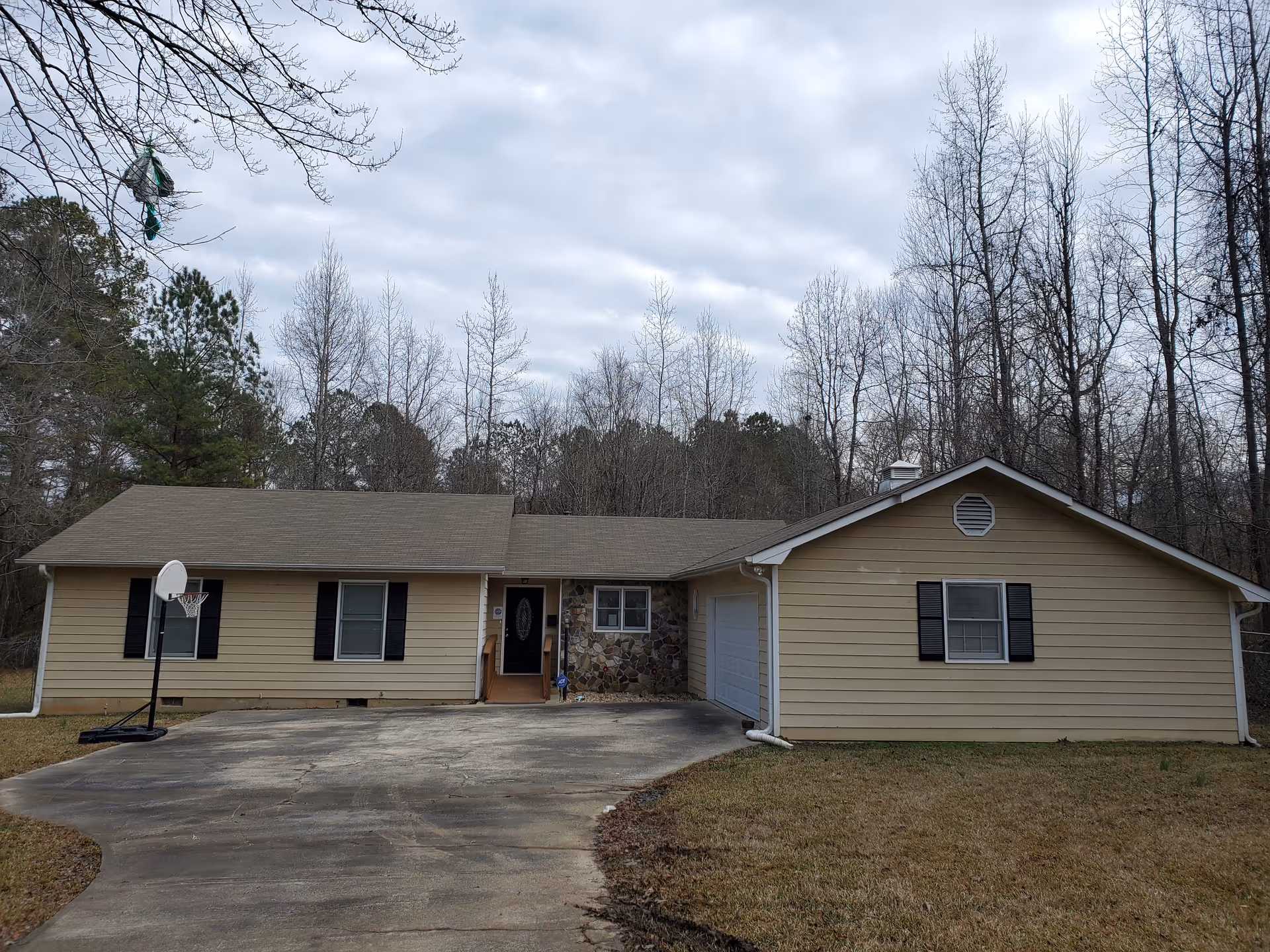 Single-story beige house with driveway, front entrance, and bare trees in a rural setting.