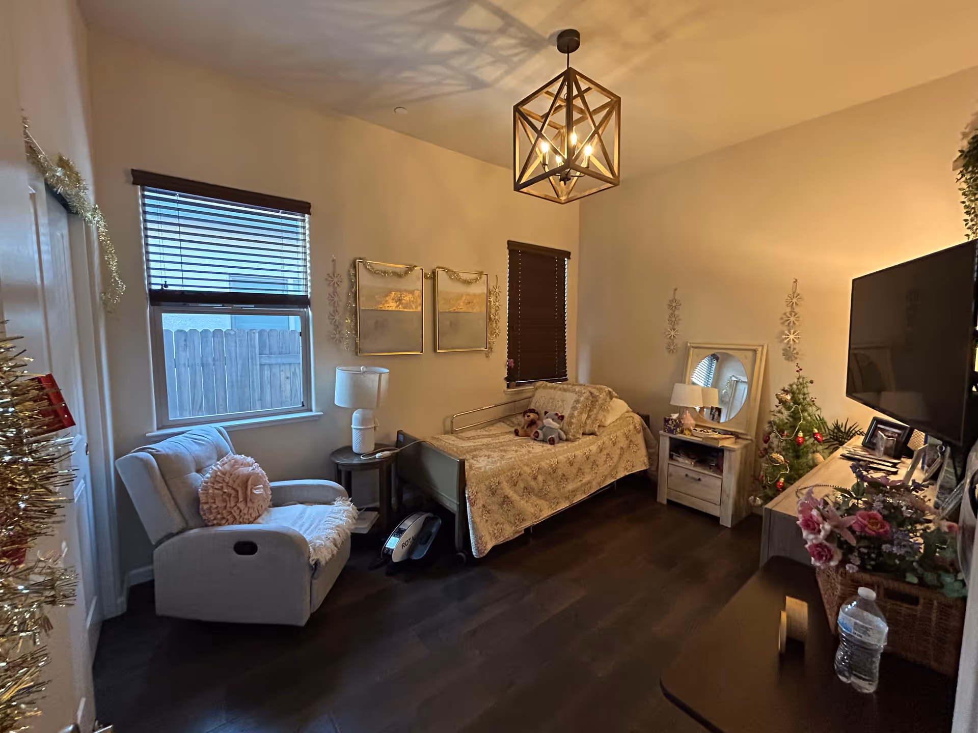 Cozy bedroom with bed, chair, dresser, small Christmas tree, and festive decor.