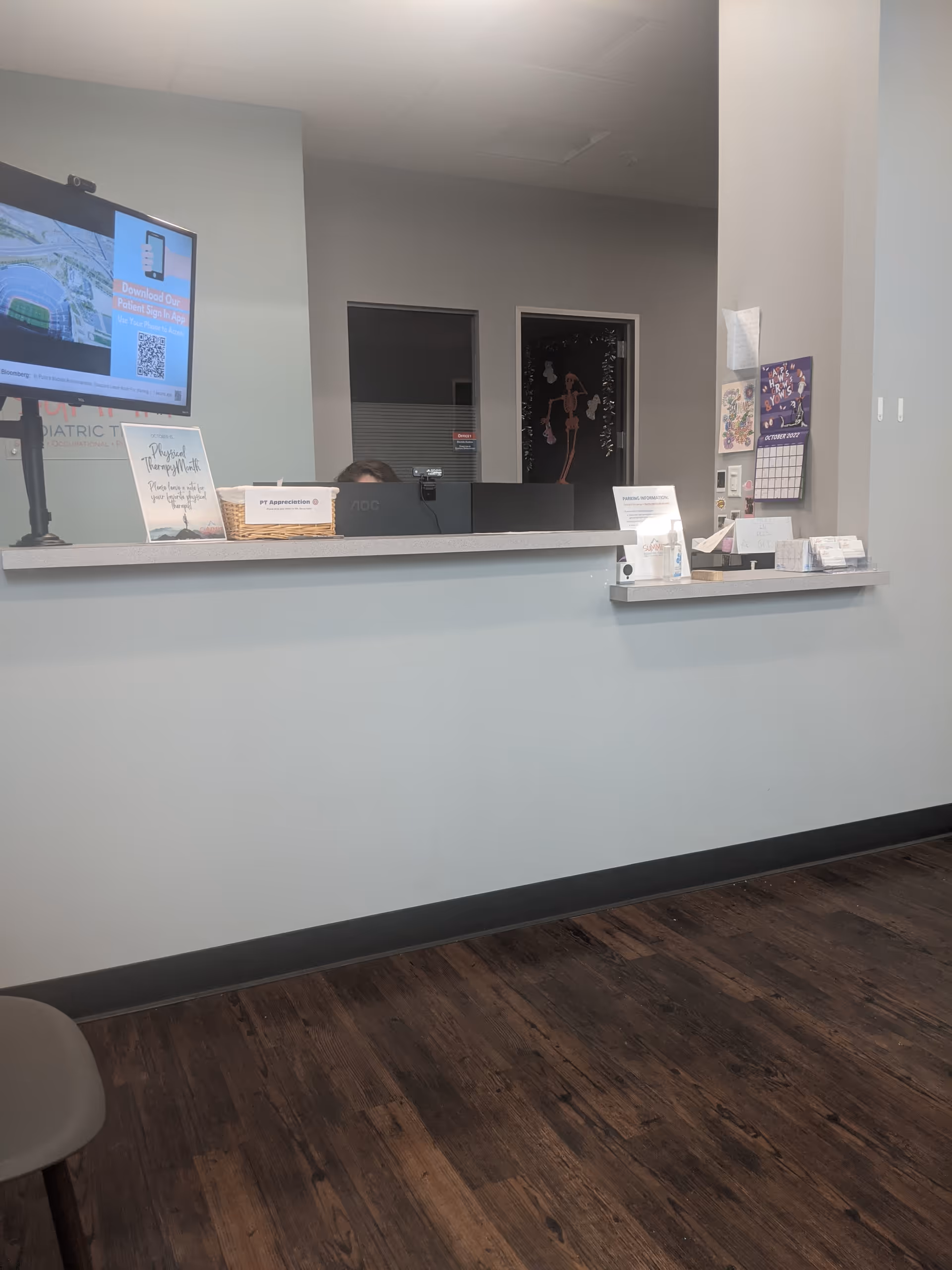 Reception desk in a clinic lobby with computer and brochures on a wood floor.