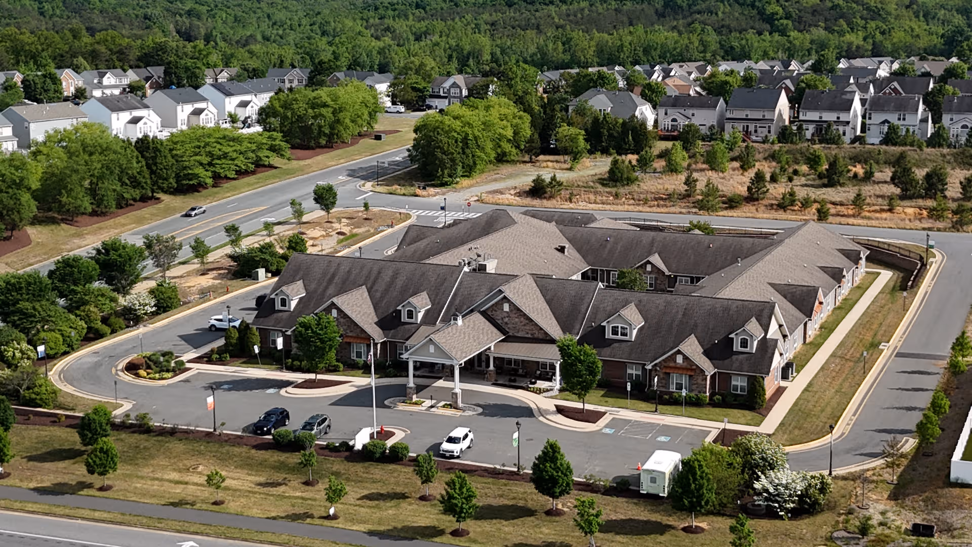 A large, multi-wing senior living facility with parking and surrounding trees.