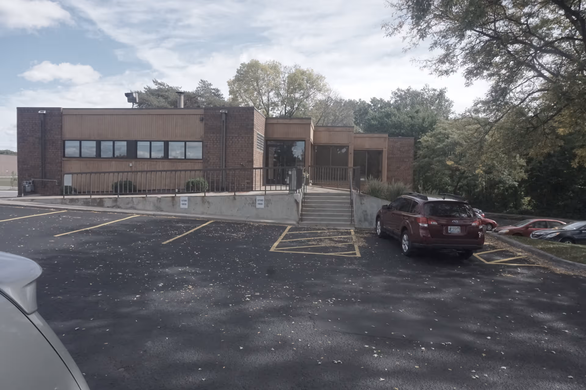 Exterior view of a brick facility entrance with steps and parking lot.