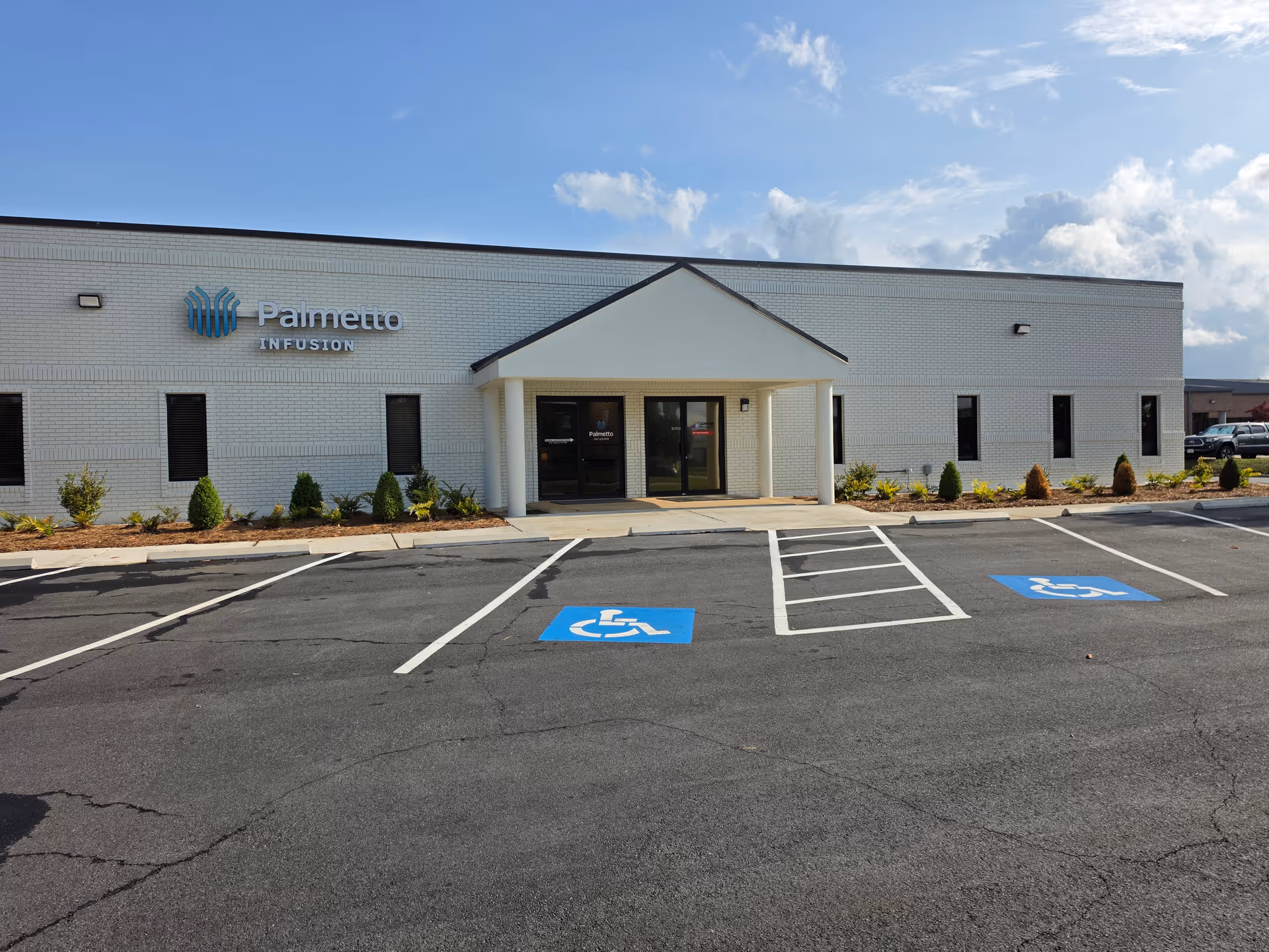 White brick facility front with Palmetto Infusion sign, handicap spots, clear blue sky