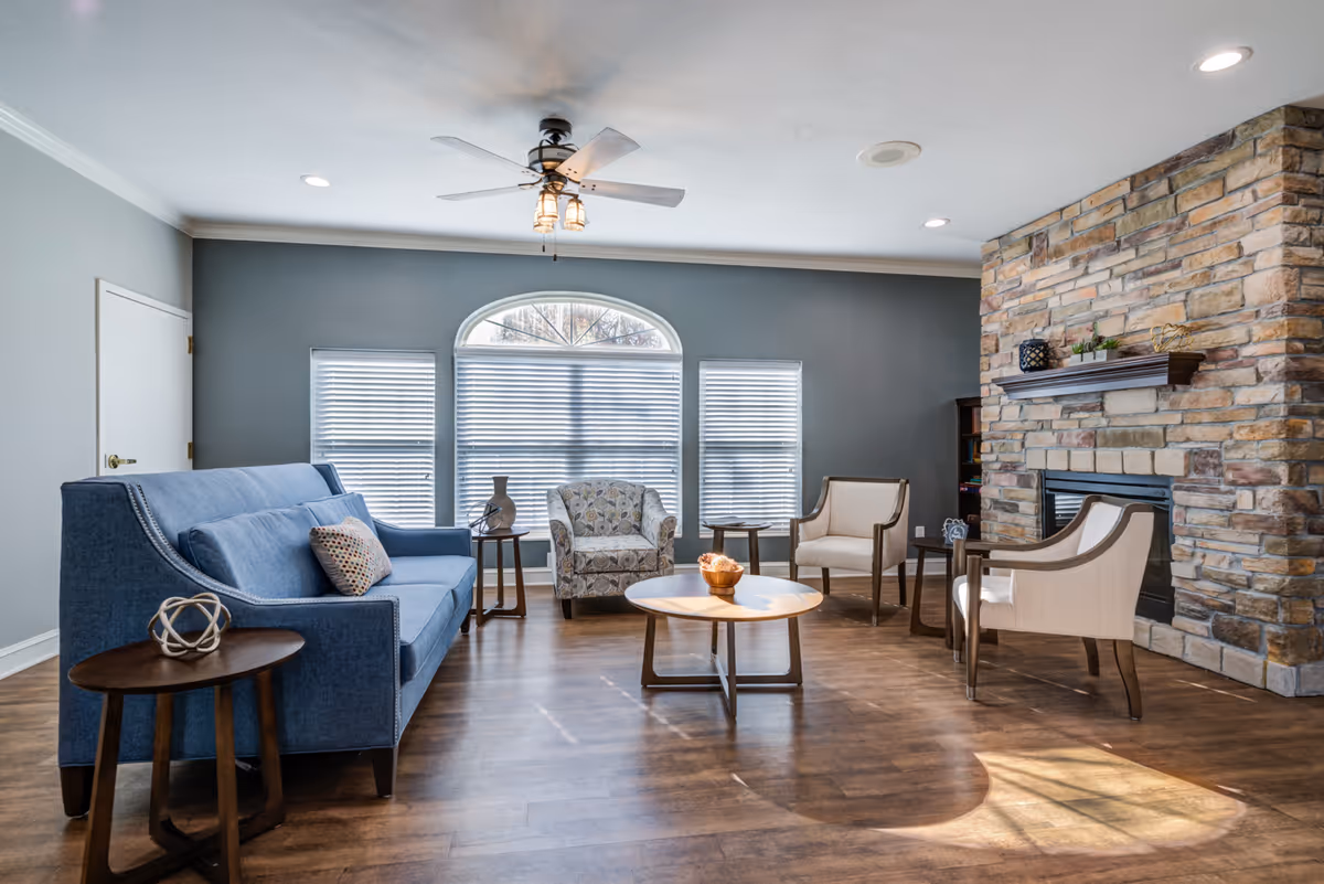 Cozy living room with blue sofa, chairs, round coffee table, large windows, and stone fireplace.
