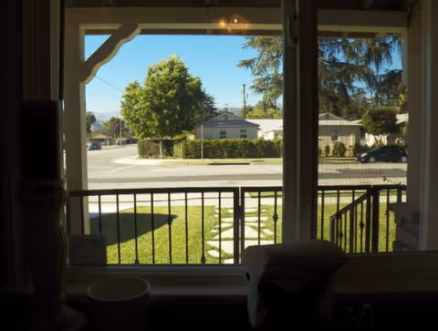 View from inside a porch looking out at a sunny street with trees