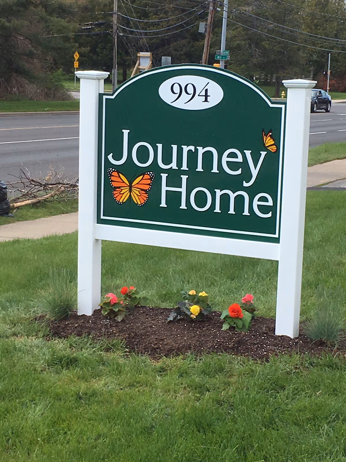 Green Journey Home sign with butterflies on posts, planted flower bed, grassy lawn.