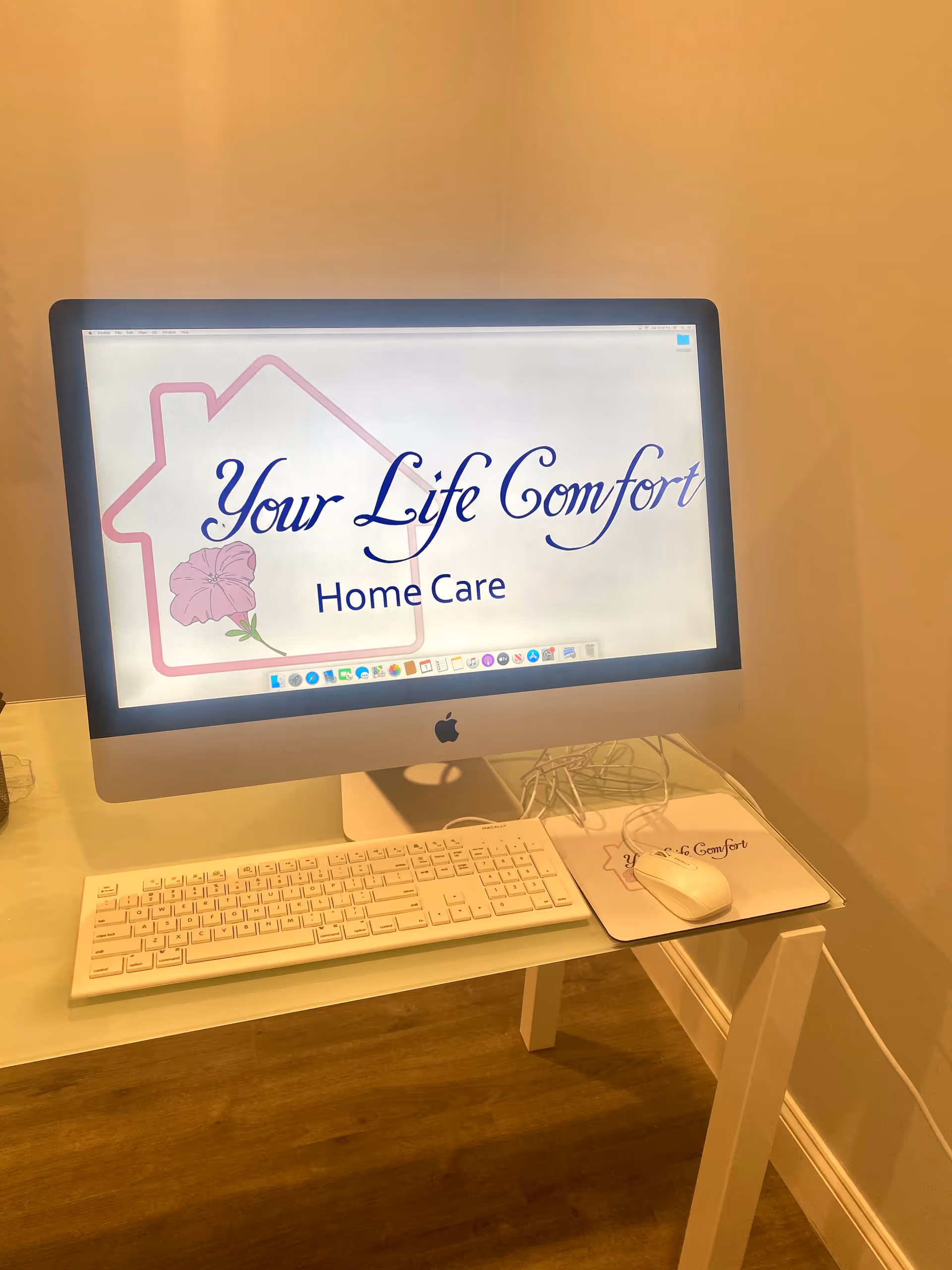 An Apple iMac on a desk displays the Your Life Comfort Home Care logo