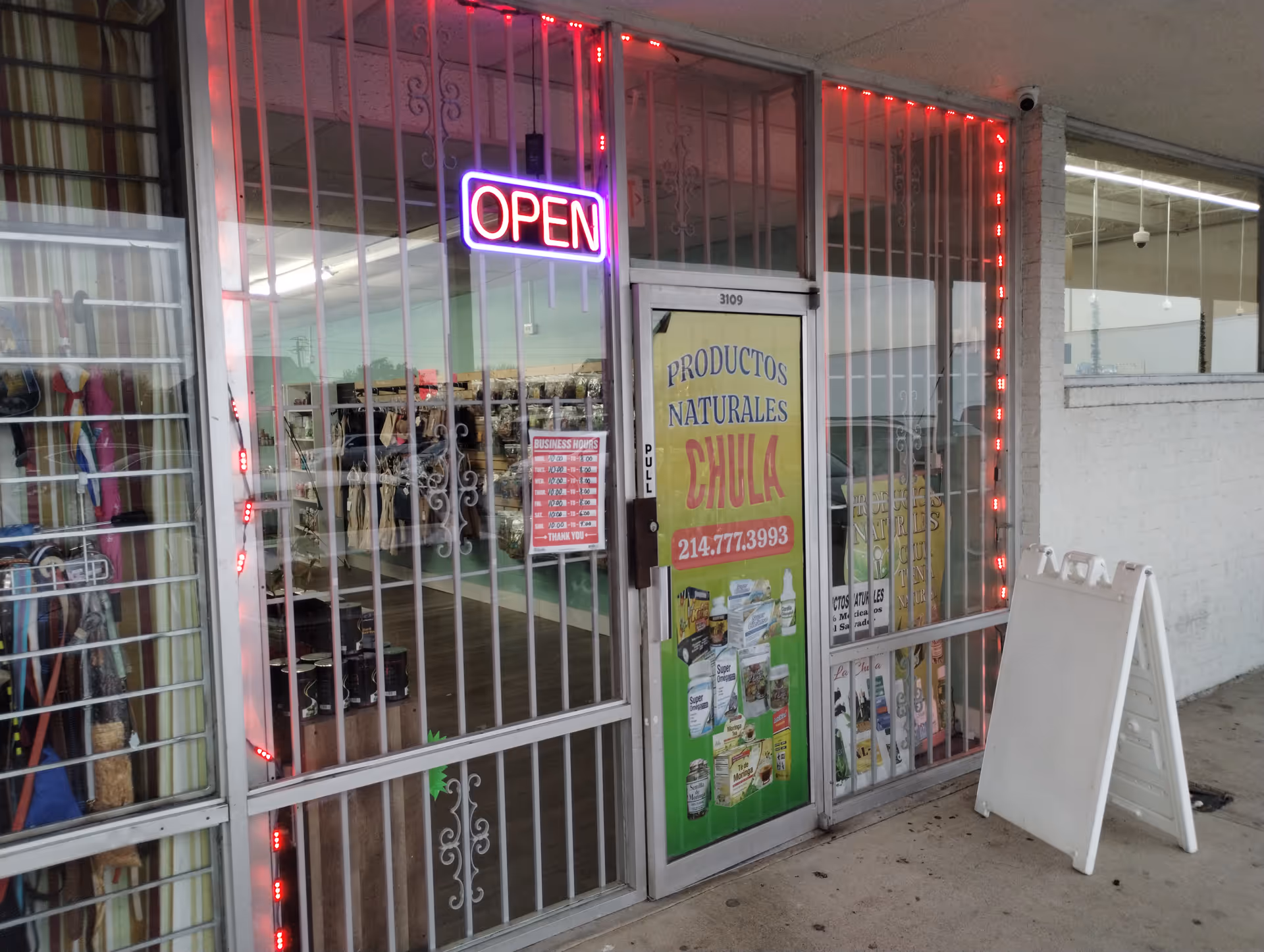 Storefront for Productos Naturales Chula with neon OPEN sign and barred glass doors