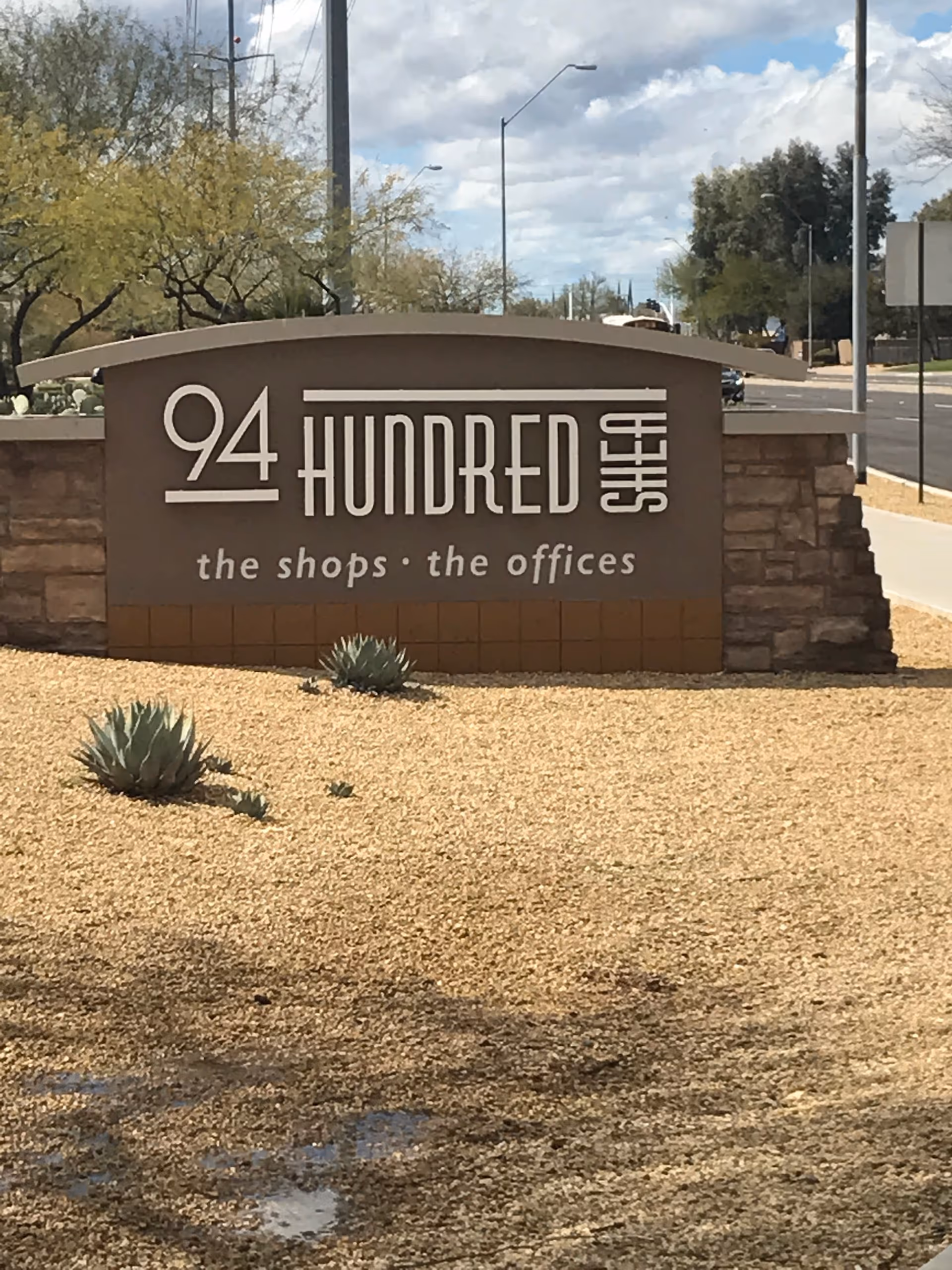 Outdoor entrance sign with desert landscaping and gravel foreground.