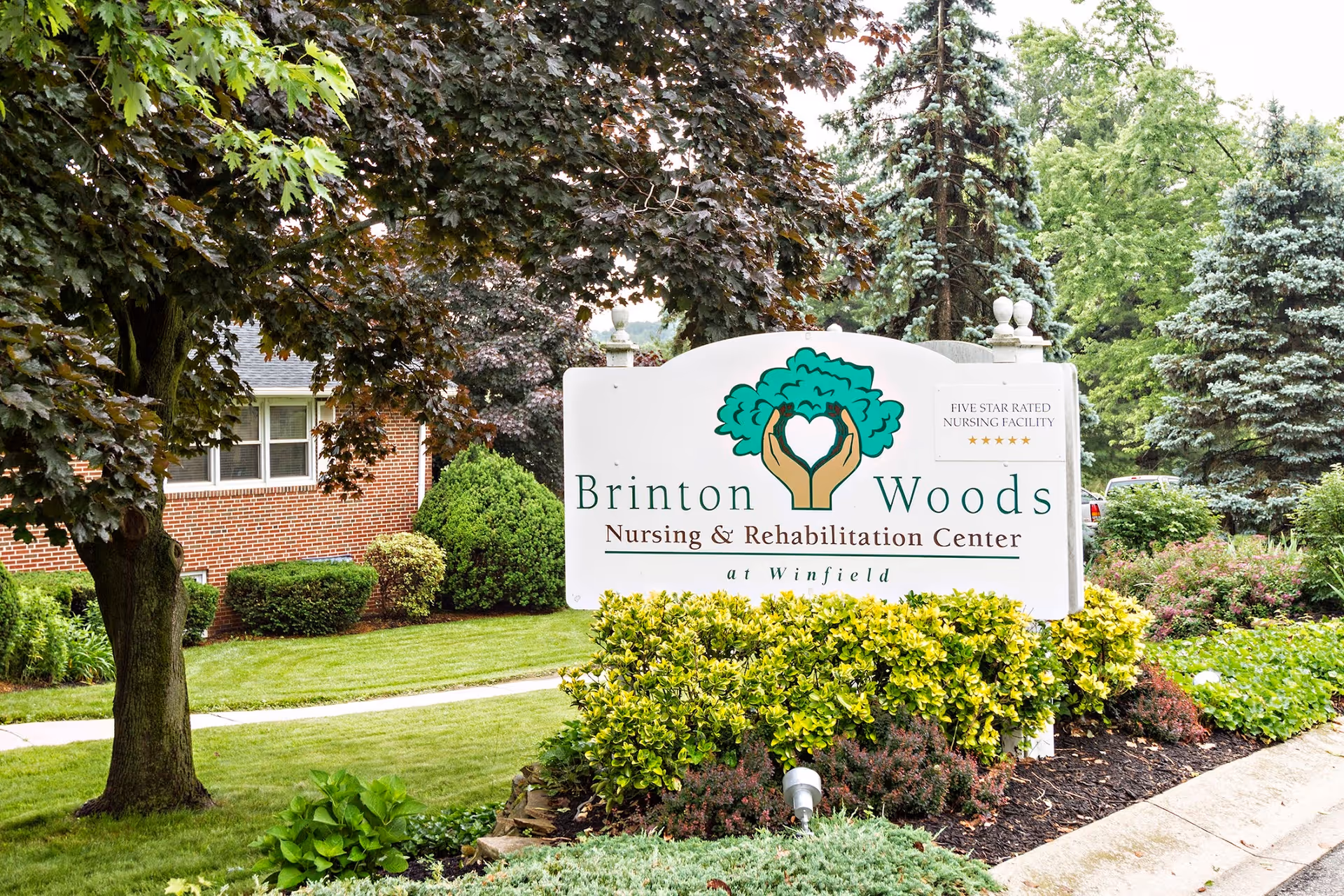 Landscaped front yard with a large sign reading "Brinton Woods Nursing & Rehabilitation Center at Winfield" in front of the building.