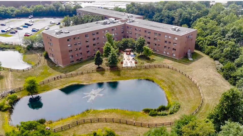 Aerial view of The Village at Eastgate Retirement Community's brick U-shaped building with a pond.