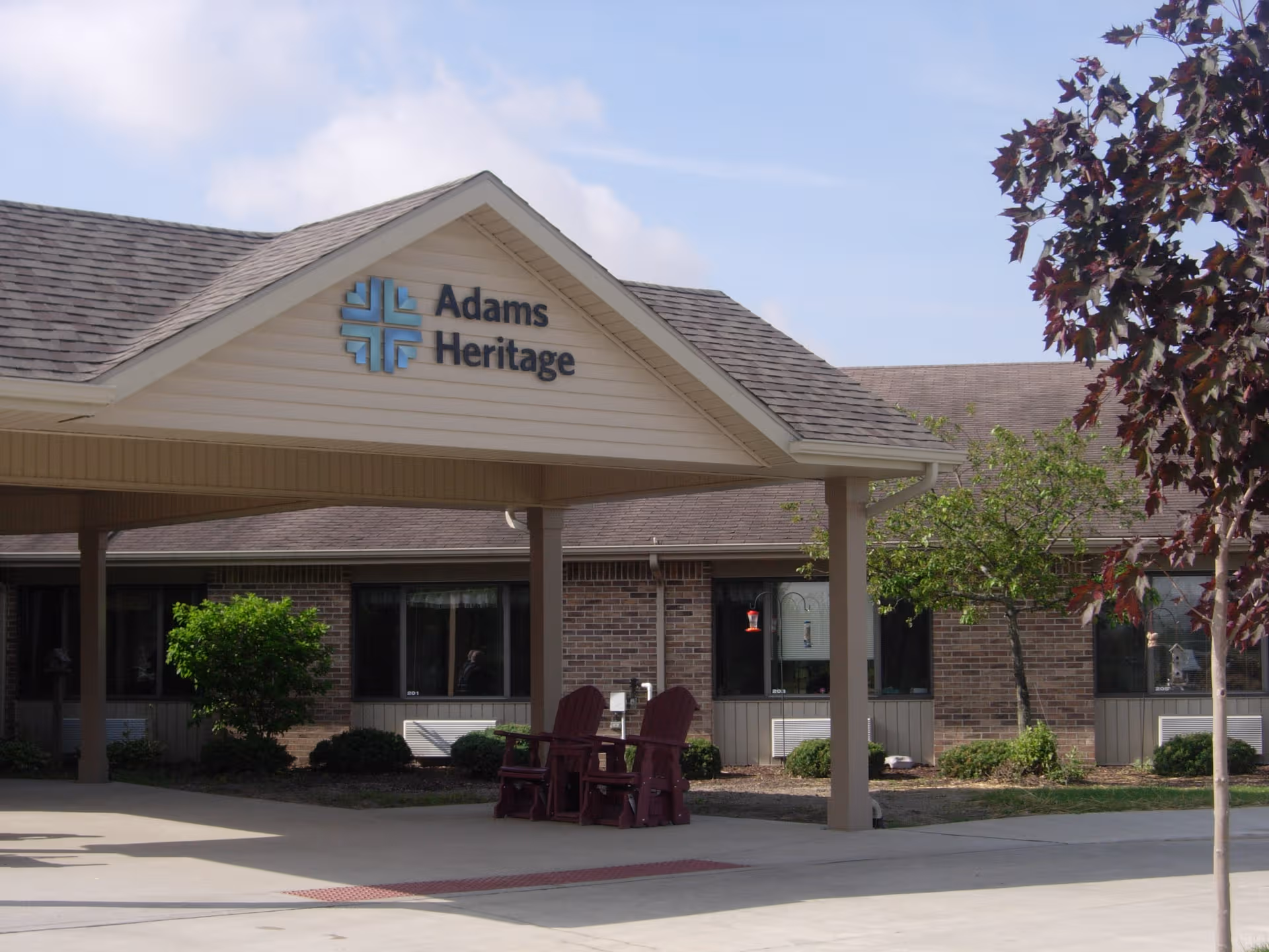Exterior view of Adams Heritage senior living facility with covered entrance and seating.