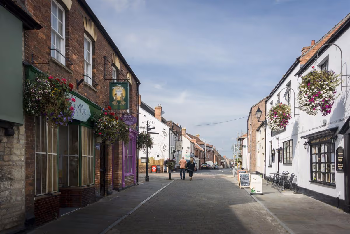 Charming town street with storefronts, hanging flower baskets, and pedestrians.