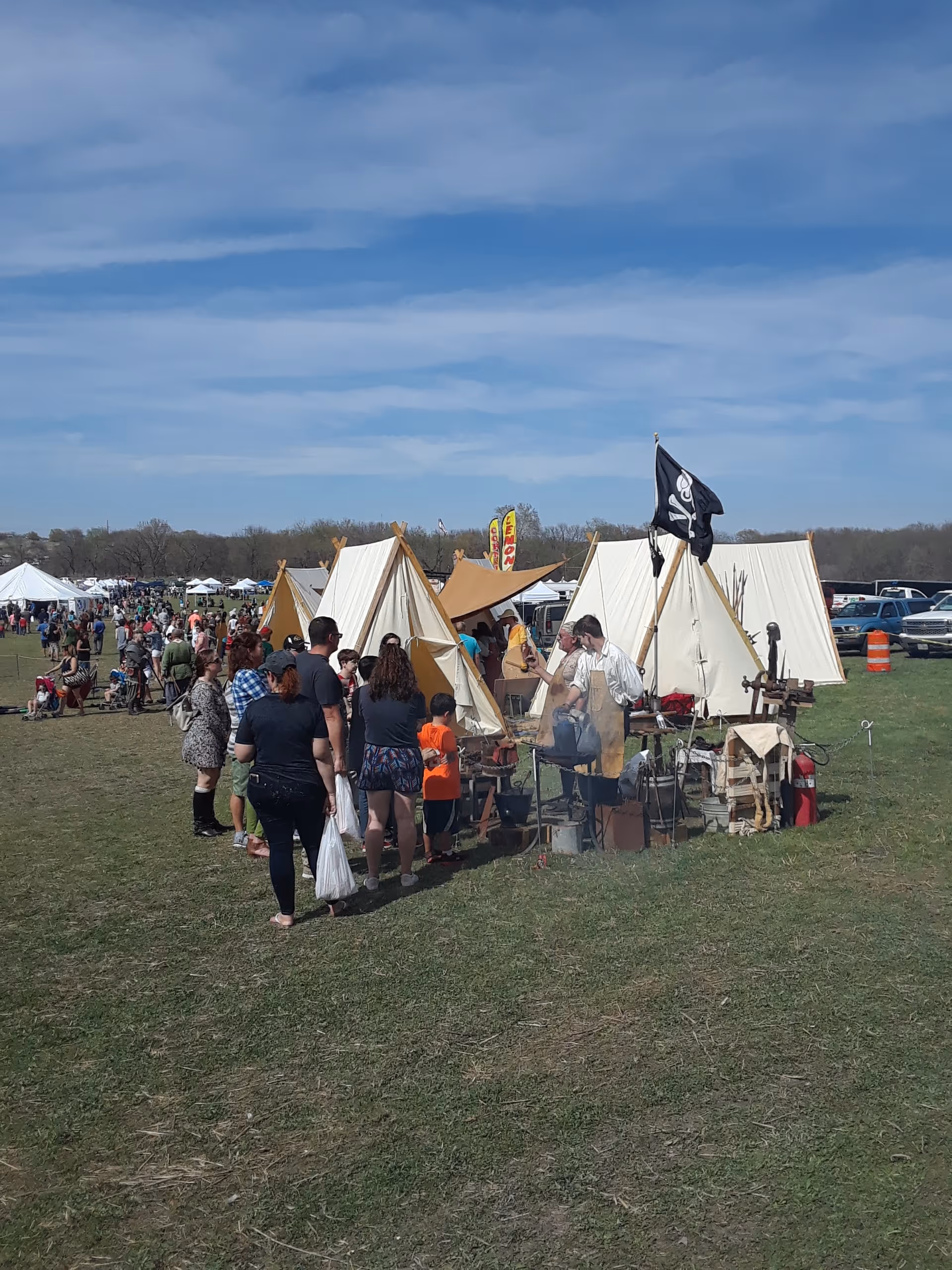 Outdoor festival with beige tents and people gathered around a cooking booth.