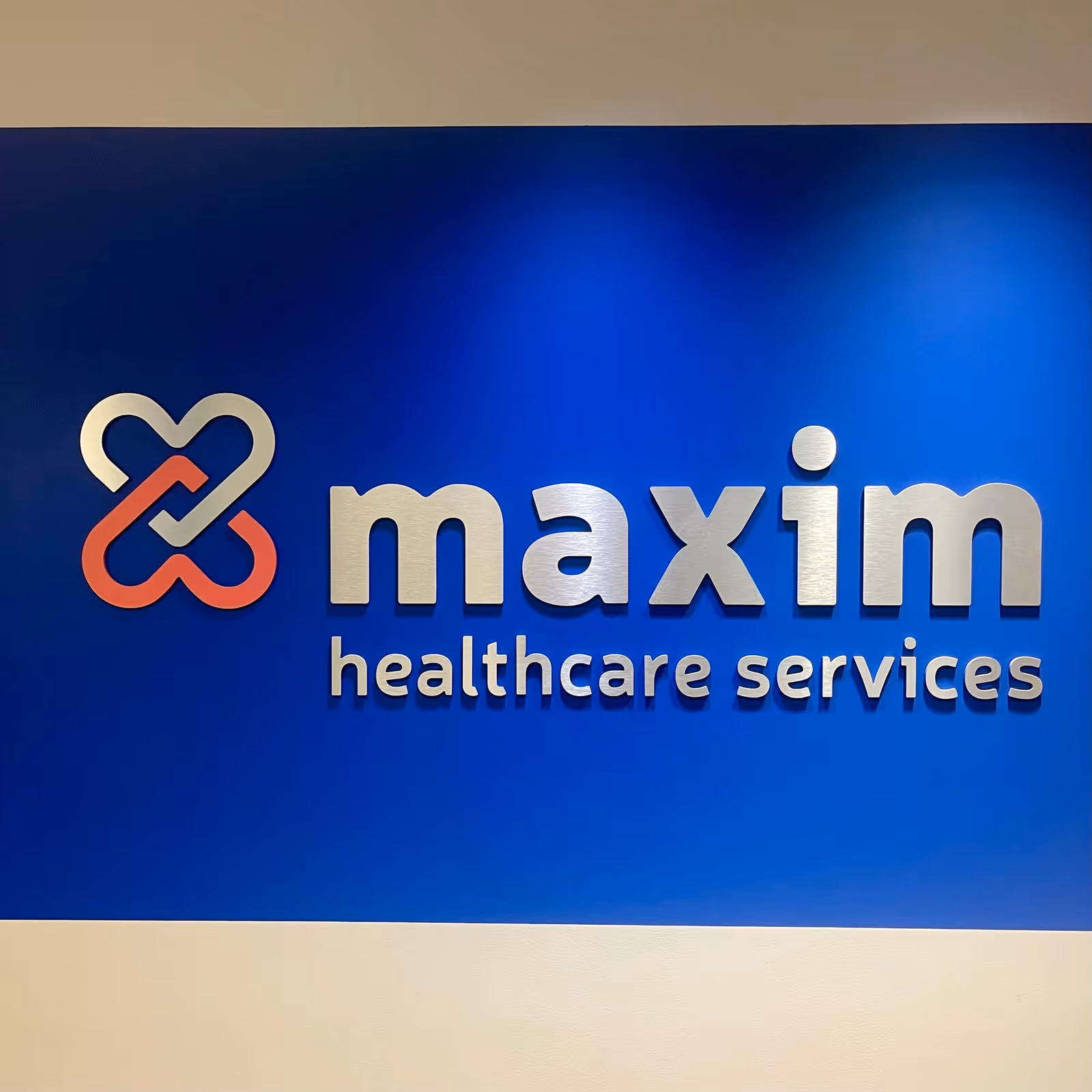 Blue wall with Maxim Healthcare Services logo and silver lettering.