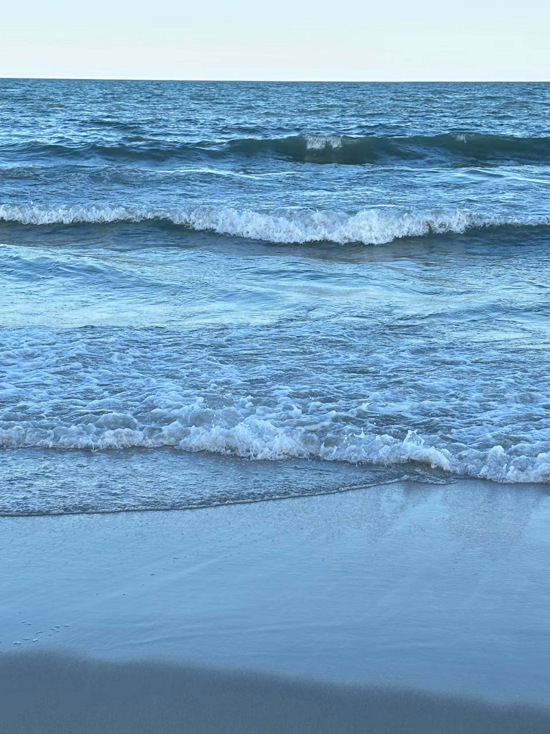 Shoreline with waves rolling onto wet sand along the blue ocean.