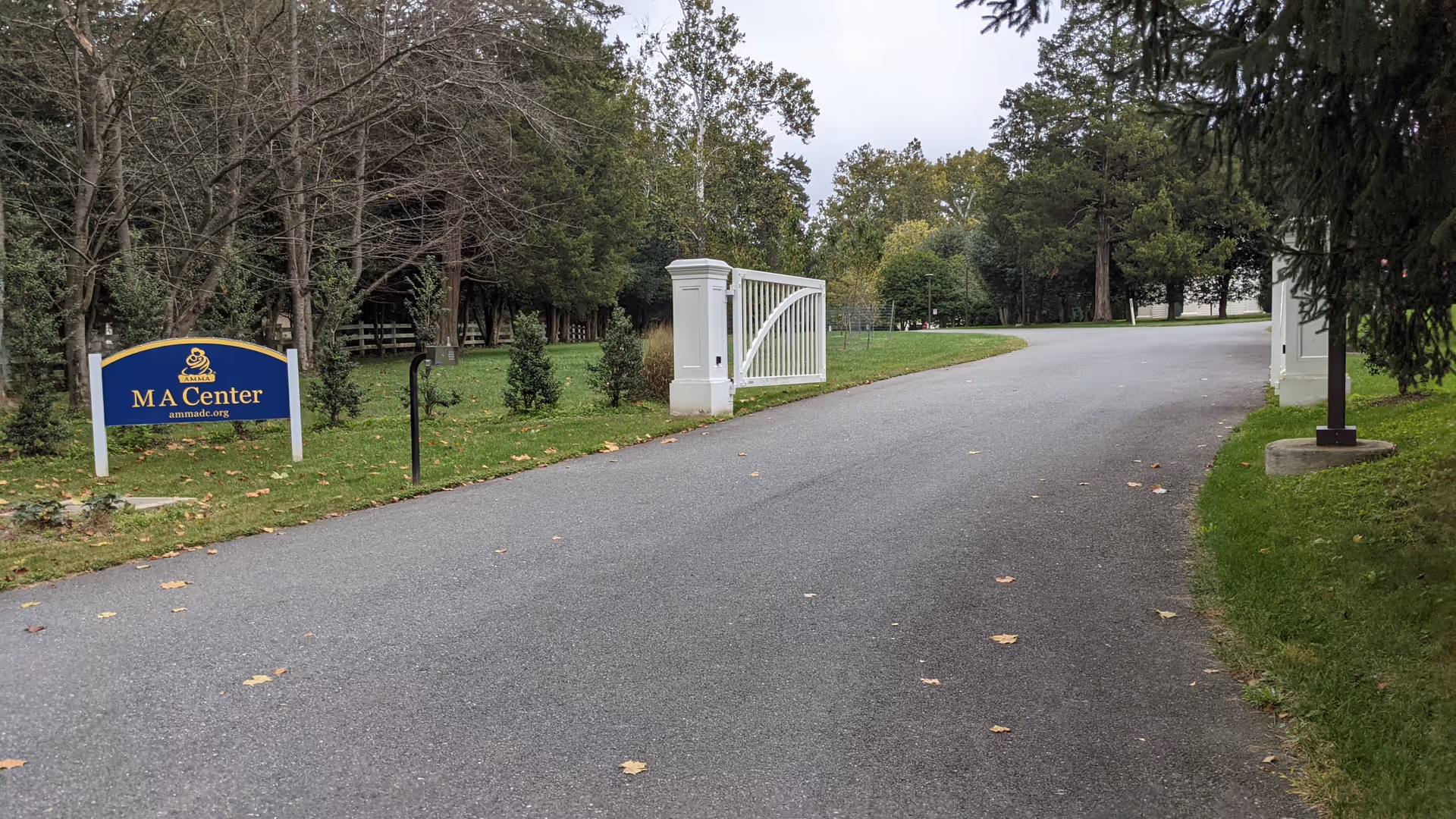 Gated driveway leads to MA Center entrance with blue sign and surrounding trees.