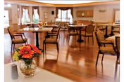 A bright dining room with wooden floors, tables, chairs, and a vase of flowers.