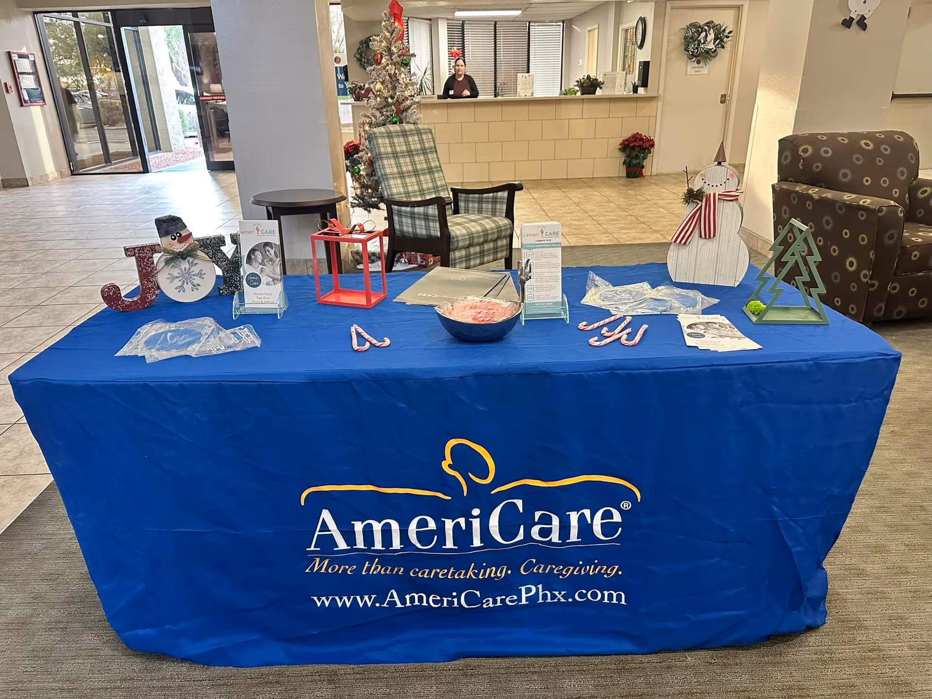 Reception area with a blue AmeriCare table, holiday decorations, and a front desk in background.