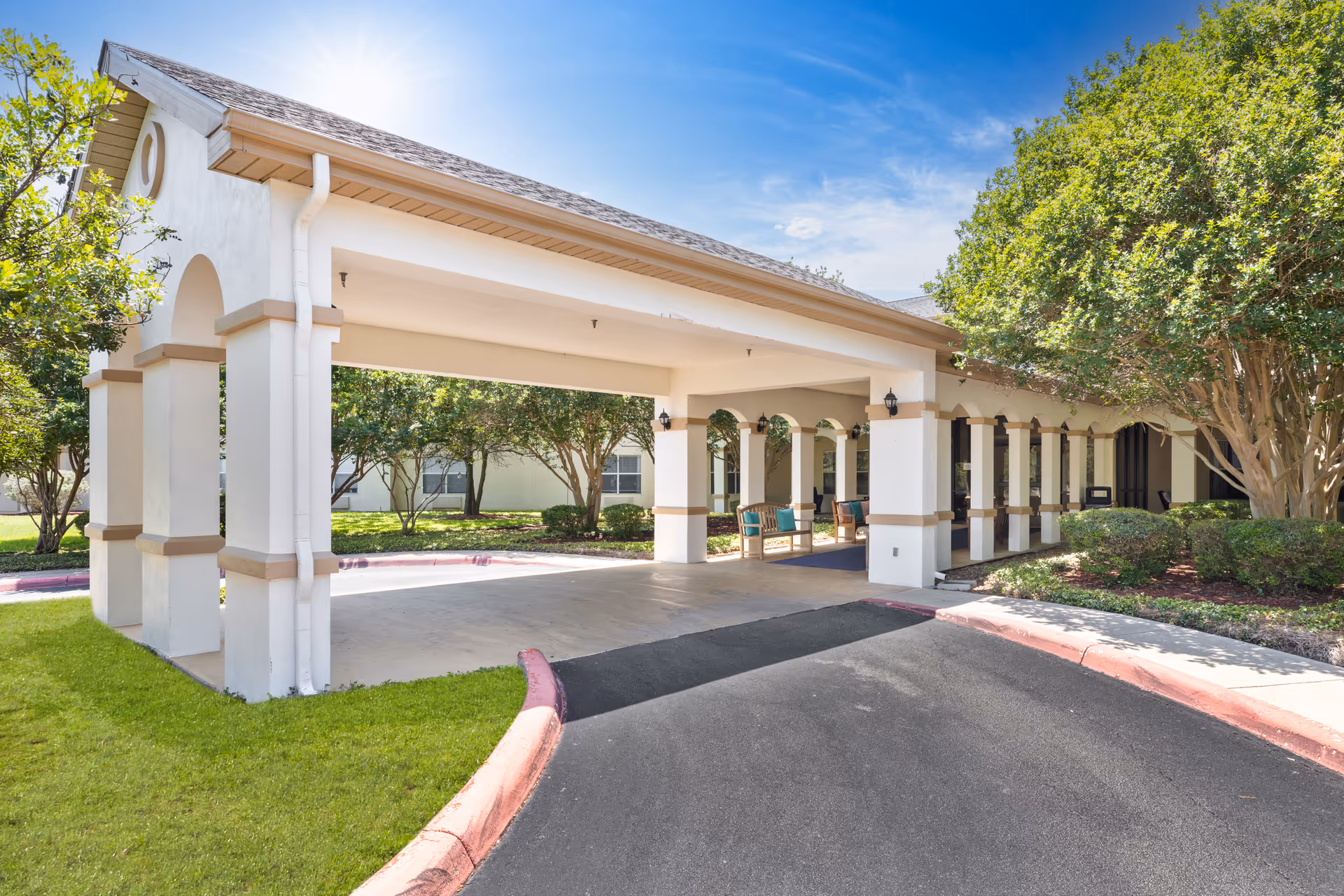 White senior living facility exterior with a covered entrance and surrounding landscaping
