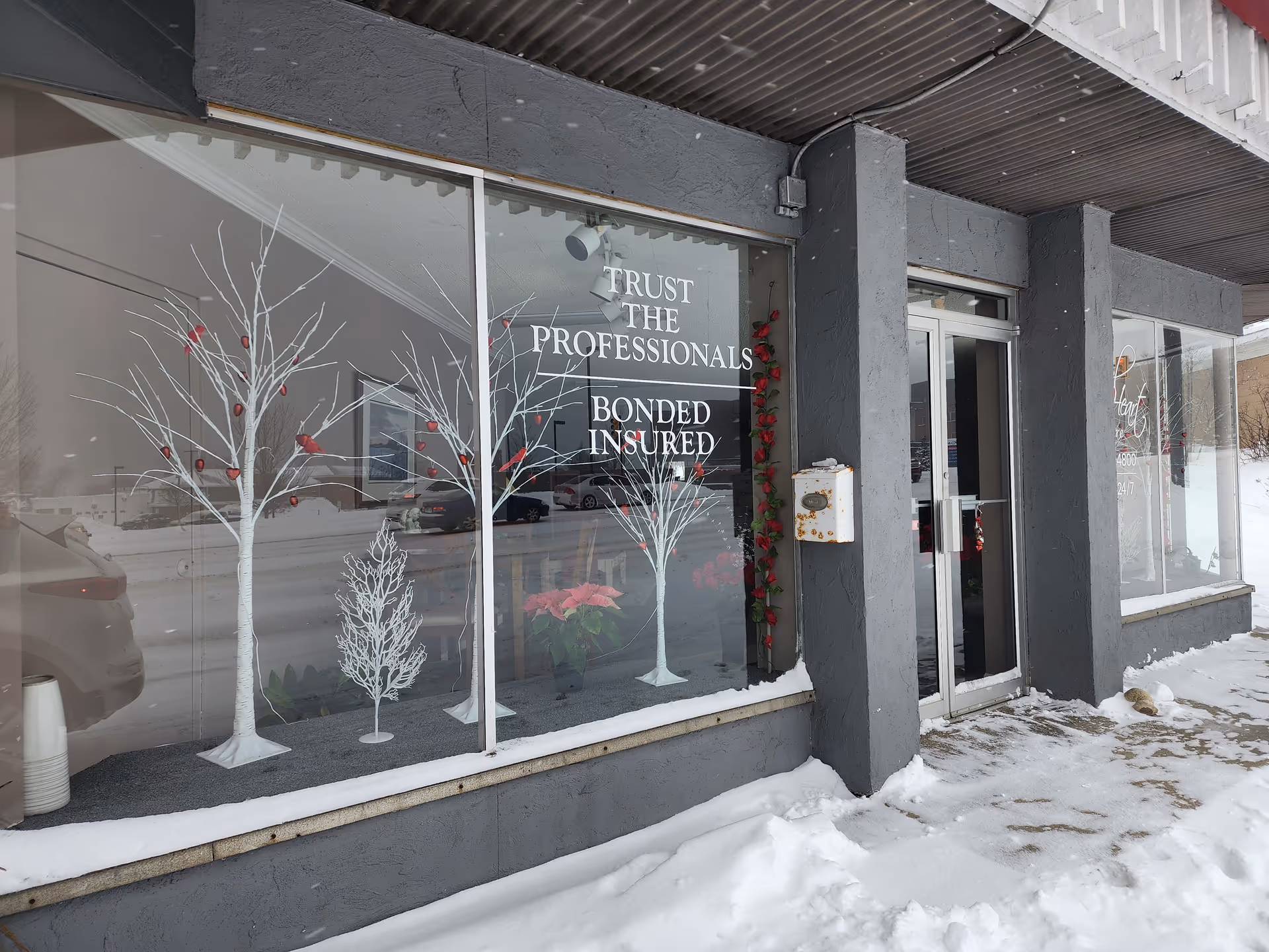 Grey storefront with large glass windows displaying Trust the professionals and winter decorations.