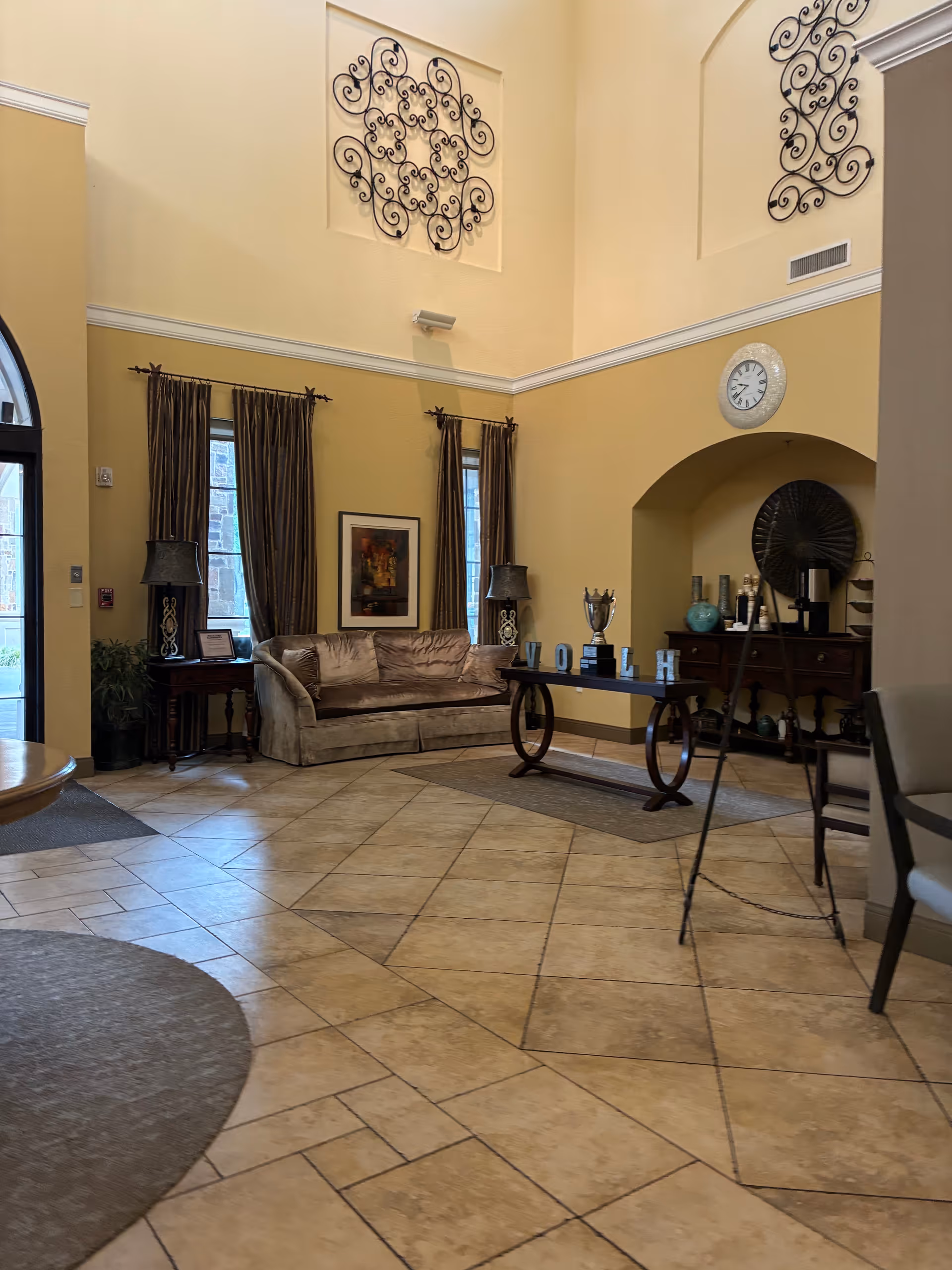 Senior living lobby with beige walls, high ceiling, sofa, lamps, and decorative metal wall art.