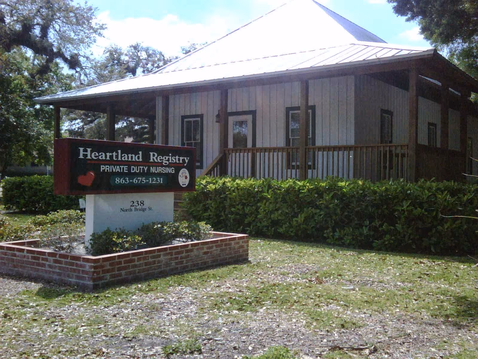Small wooden building with Heartland Registry sign, hedge, and brick planter in front.