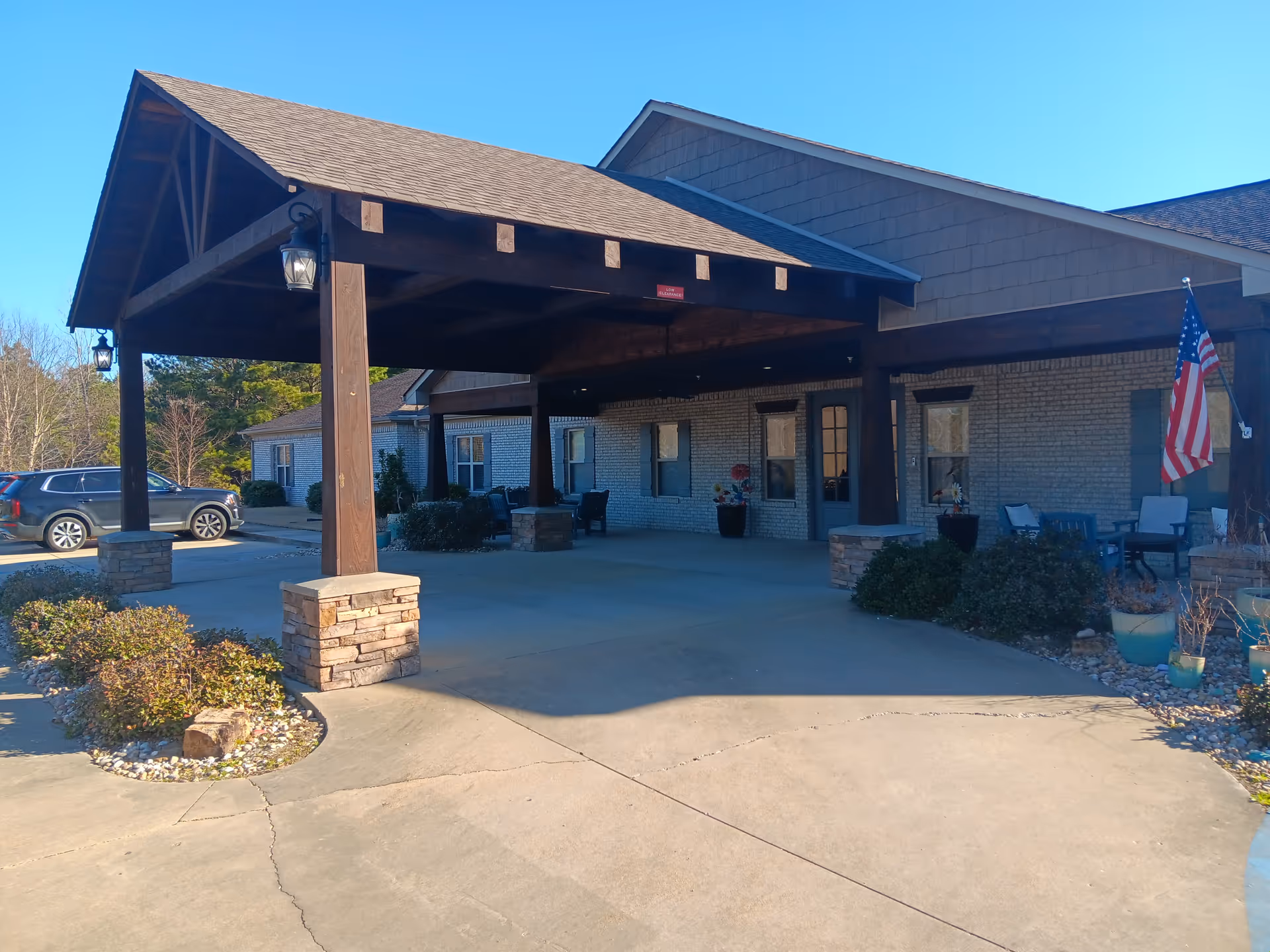 Exterior entrance of a senior living facility with a covered drop-off area and chairs.