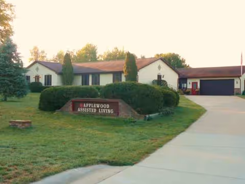Exterior view of Applewood Assisted Living with sign and manicured shrubs.