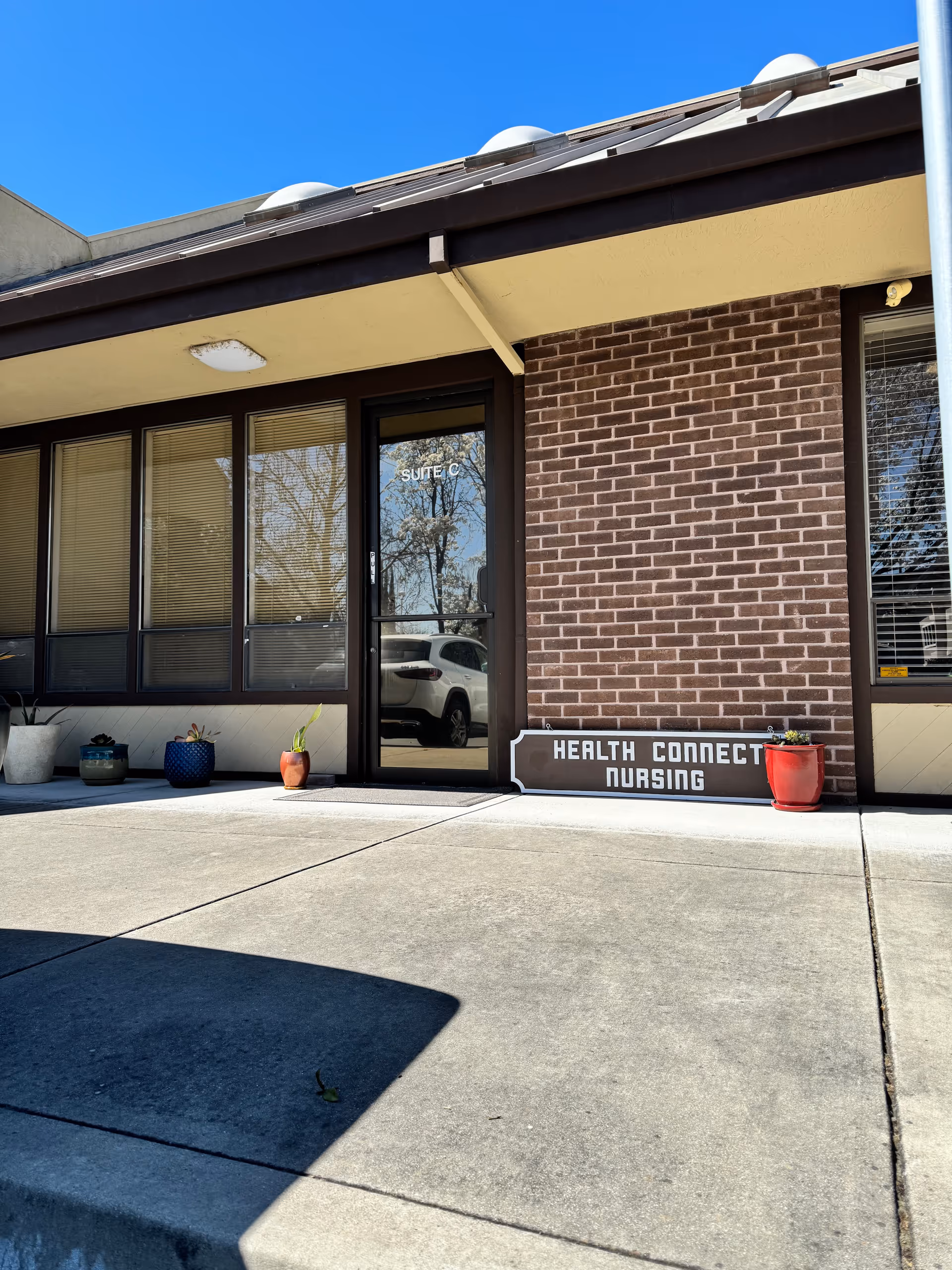 Exterior view of Health Connect Nursing entrance on brick building with potted plants.