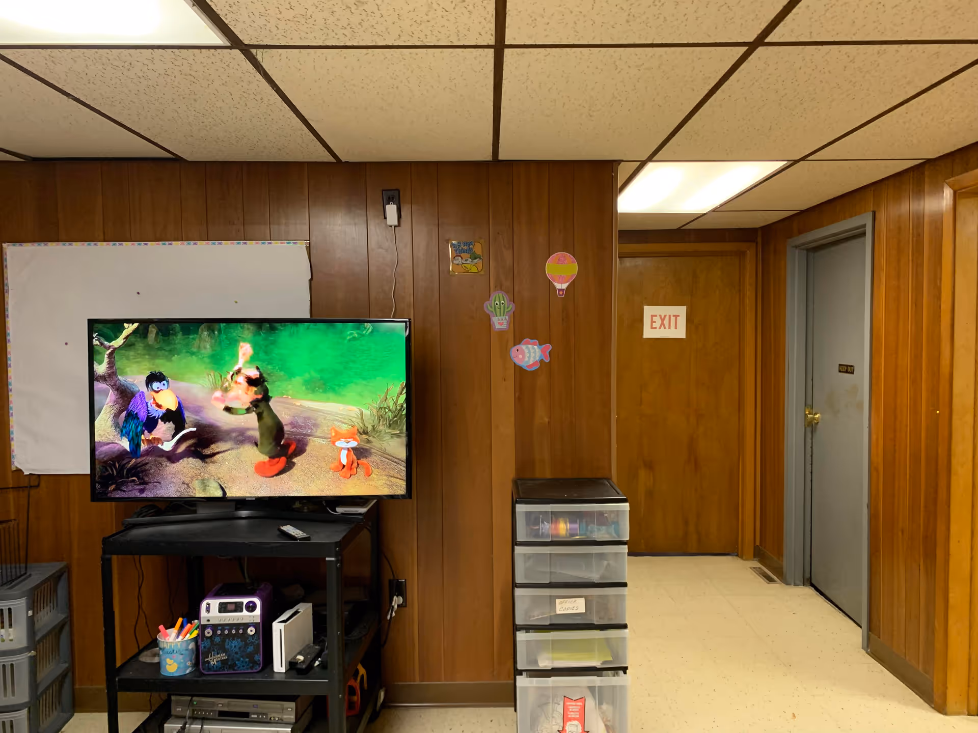 wood-paneled room with TV, drawers, exit door, and playful wall decorations